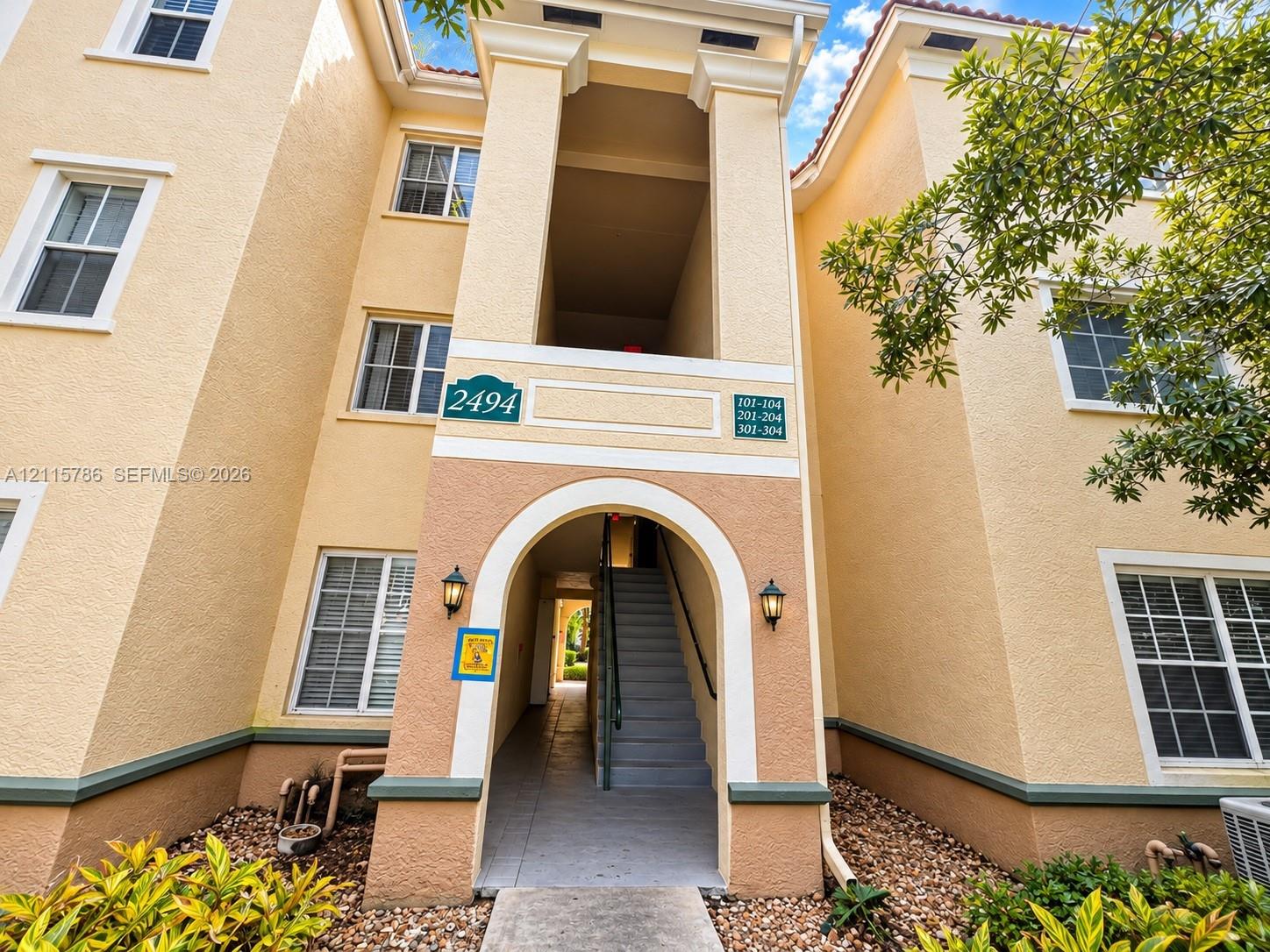 Stucco exterior featuring a prominent arched entry, tiered architectural facade, dual wall-mounted coach lights, and multi-pane windows