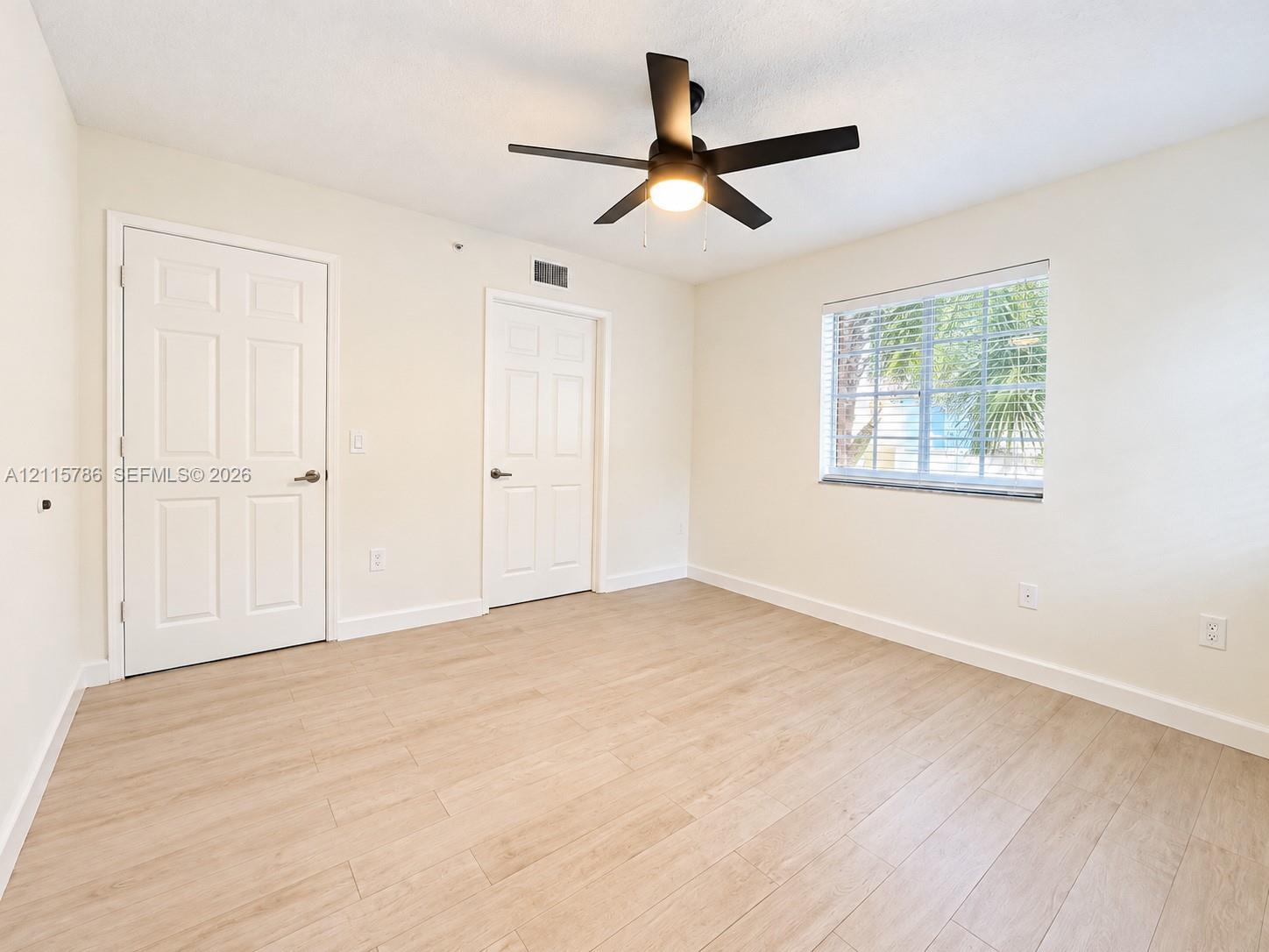 Interior space featuring wood-finish flooring, a matte black ceiling fan with an integrated light fixture, and two six-panel doors