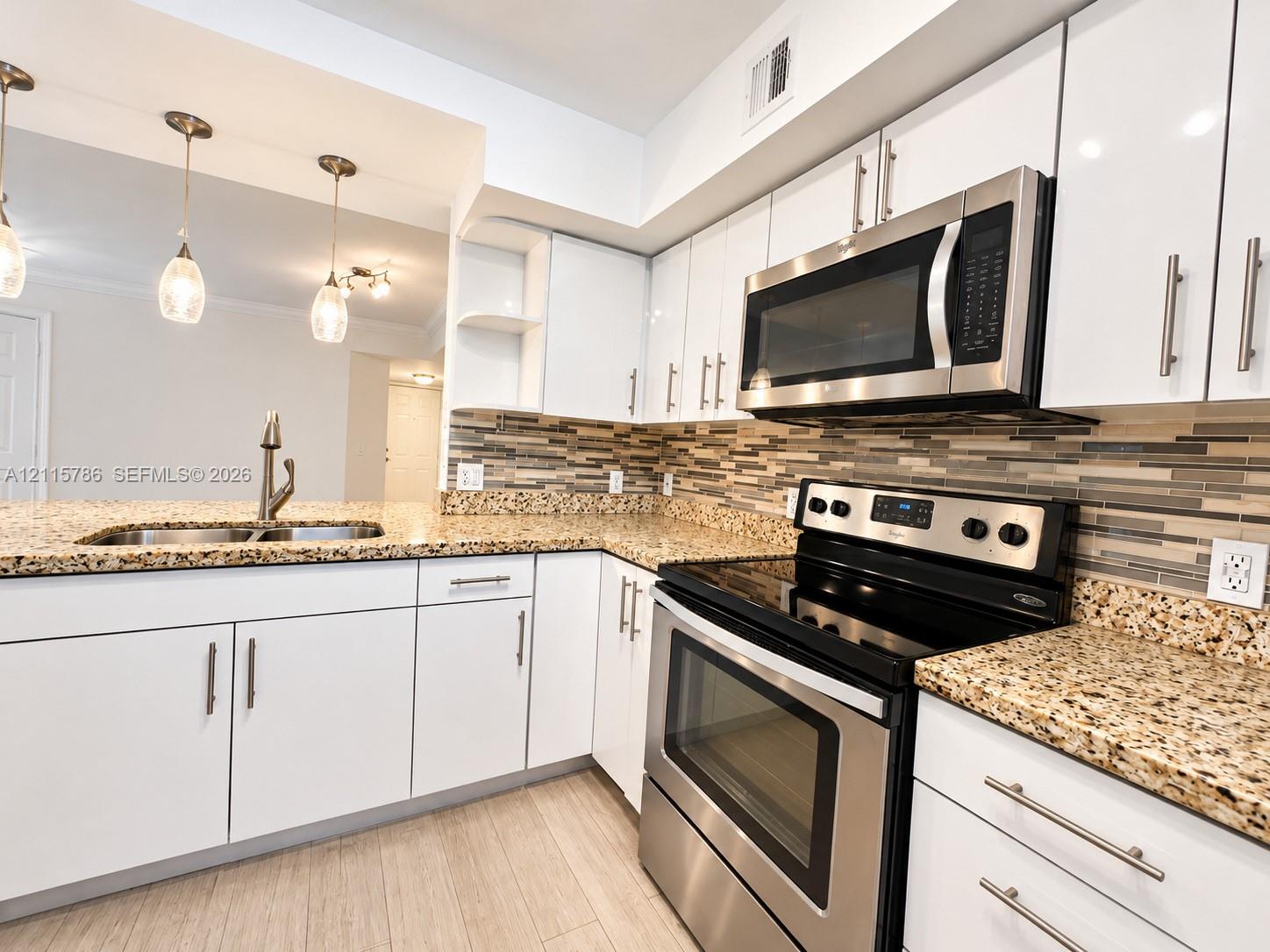 Kitchen featuring white cabinetry, stone-finish countertops, stainless steel appliances, a multi-tone tile backsplash, and overhead pendant lighting