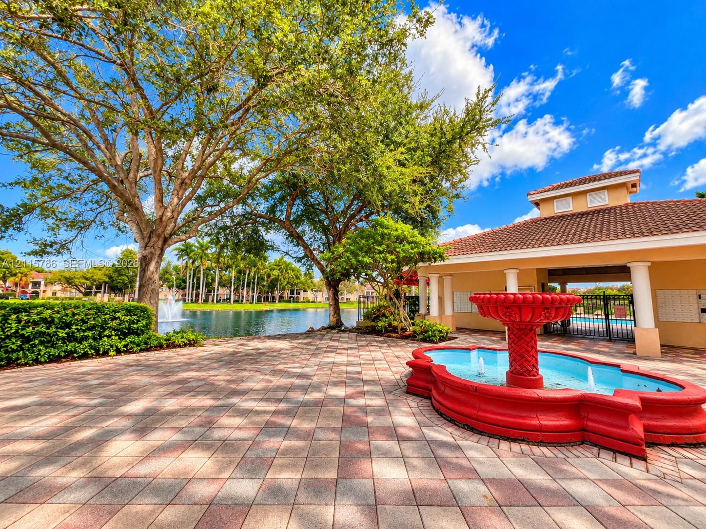 Paved courtyard featuring a decorative fountain, mature landscaping, and waterfront scenery