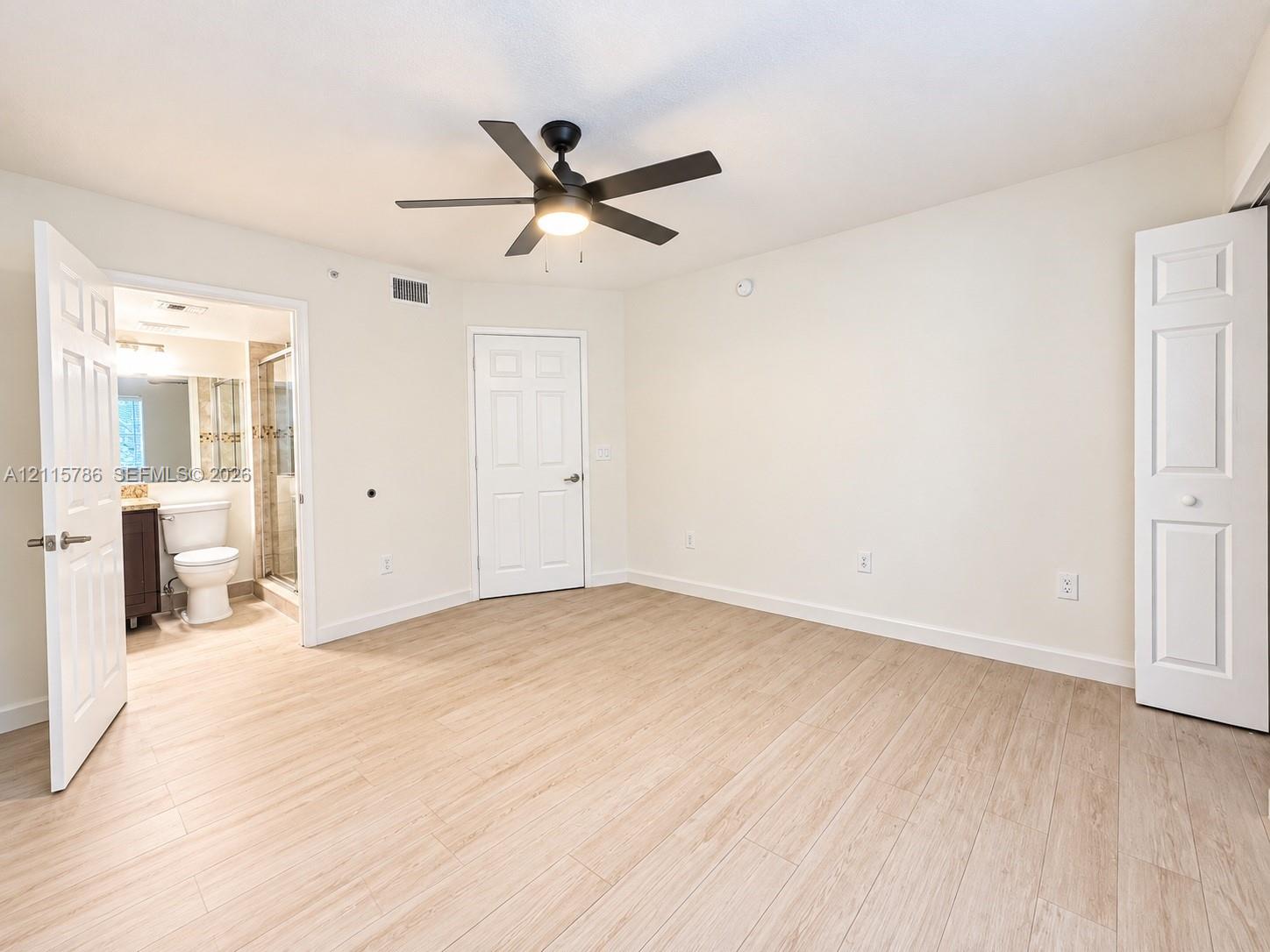 Room featuring wood-finish flooring, a central ceiling fan with integrated lighting, and white six-panel interior doors