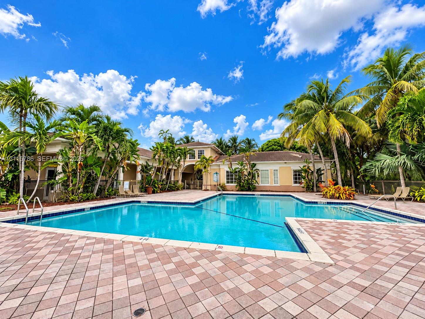 In-ground swimming pool featuring a tiled deck, stone-paver surround, metal handrails, and tropical landscaping