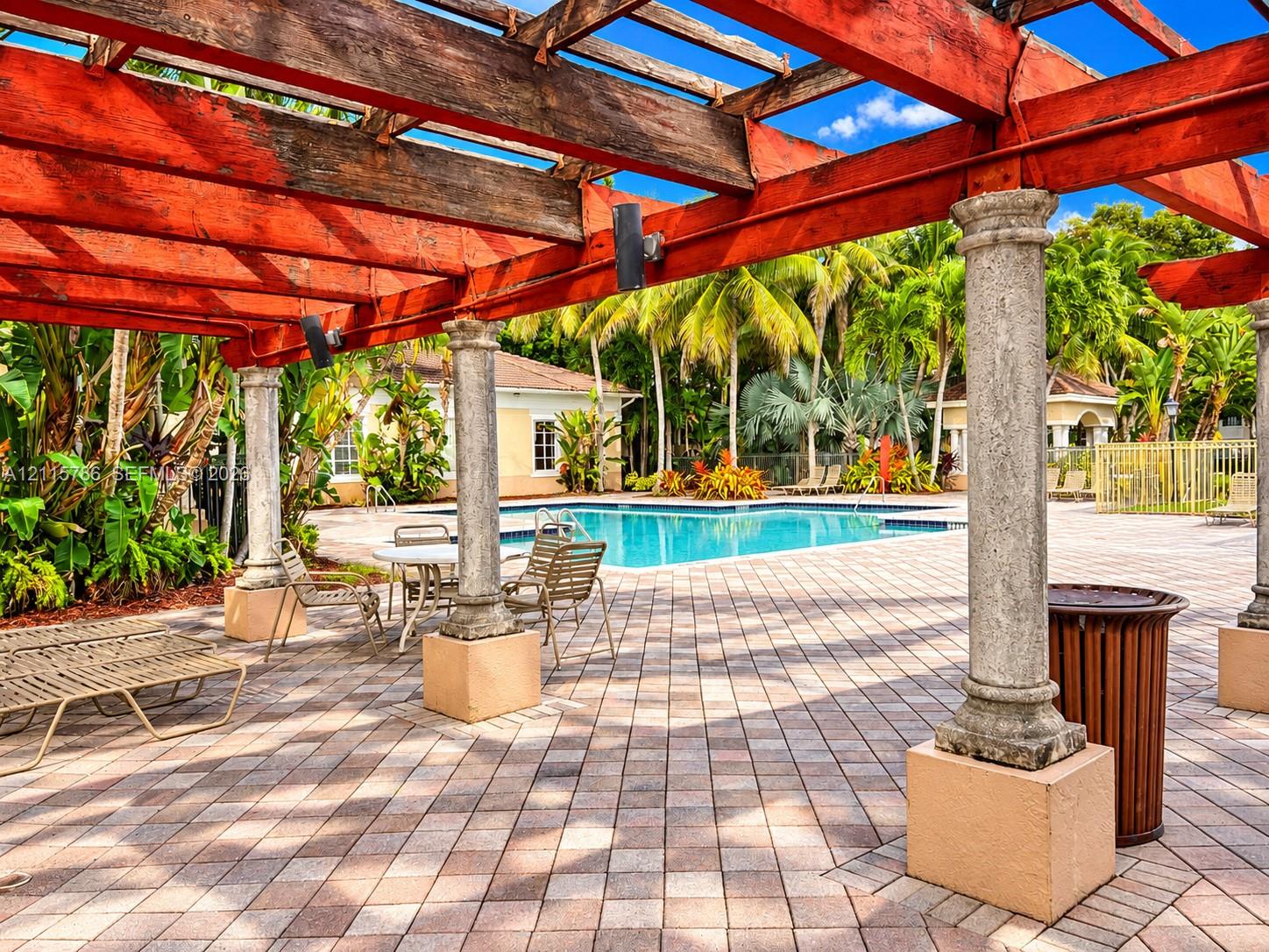 Outdoor space featuring a timber-frame pergola supported by stone-finished columns, paver patio, and swimming pool