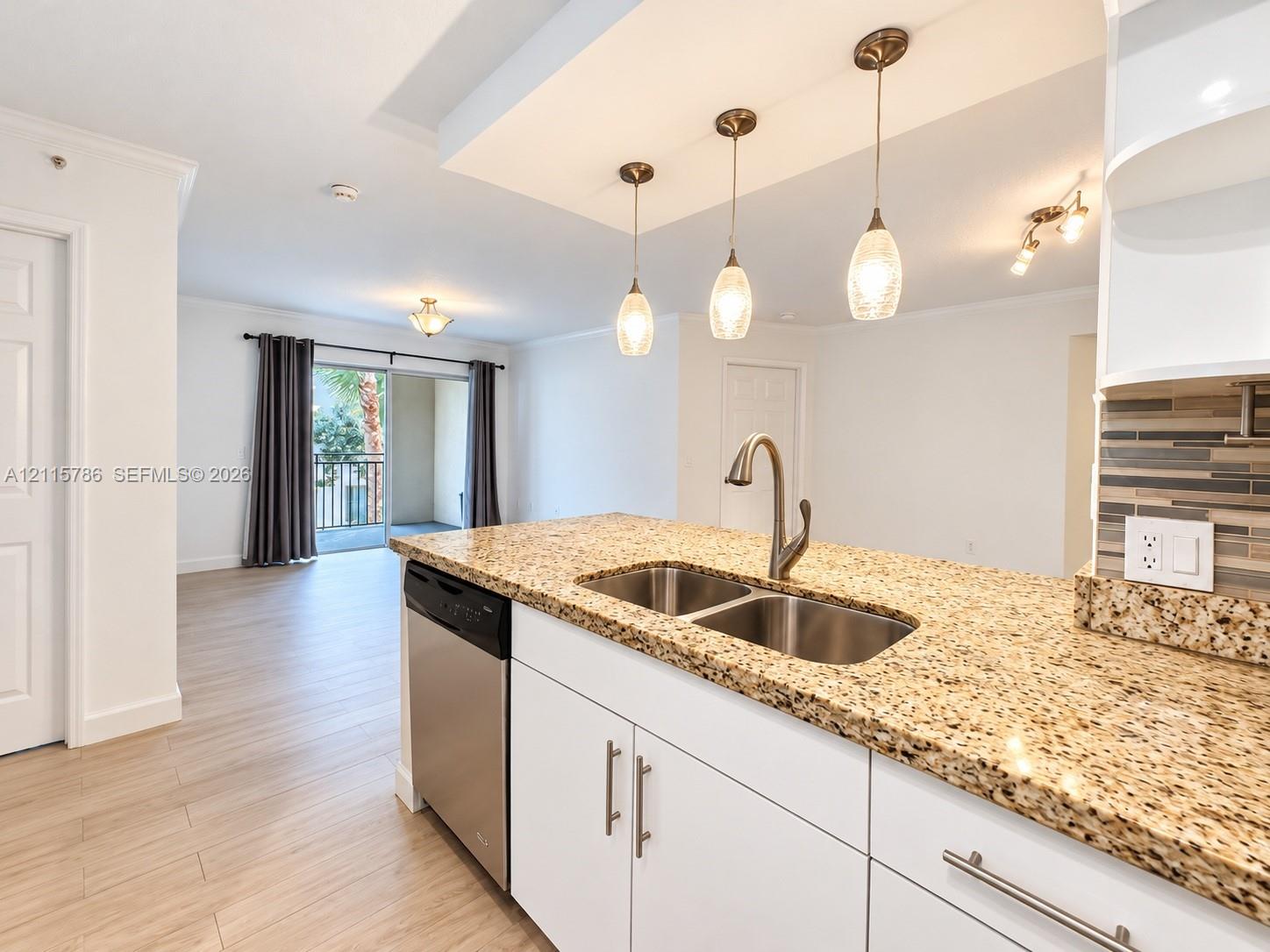 Kitchen featuring an island with stone-surface countertops, dual-basin stainless steel sink, modern pendant lighting, white cabinetry with metallic hardware, and wood-finish flooring