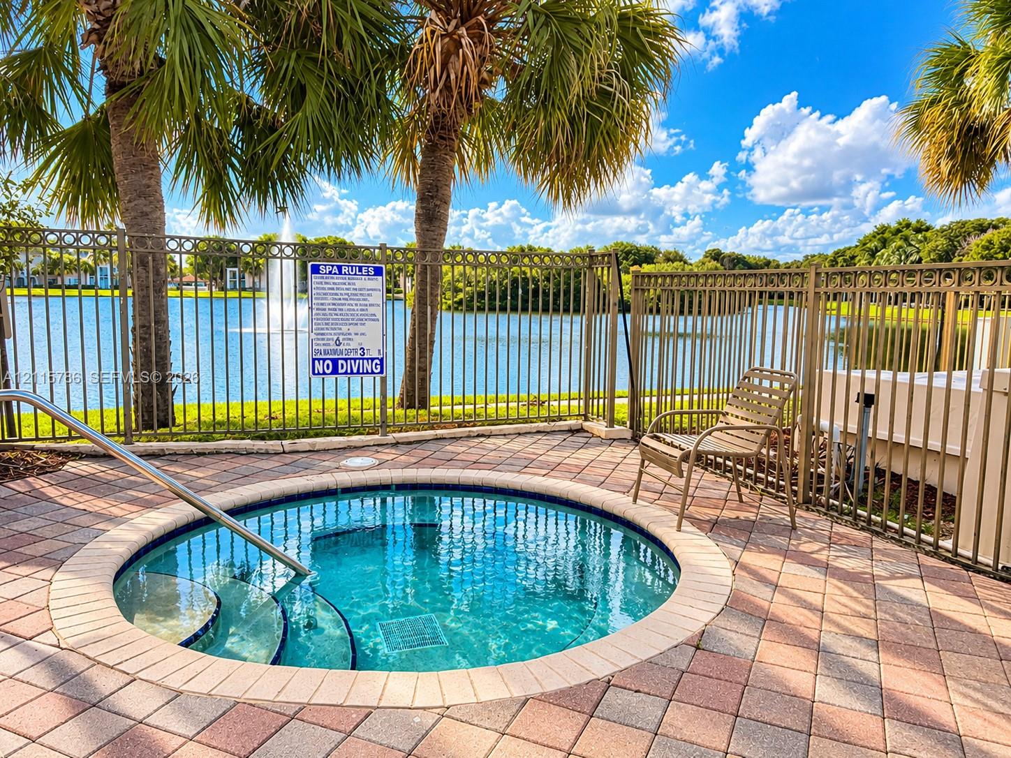 In-ground spa with stone paver surround, metal safety fencing, and palm-lined waterfront setting