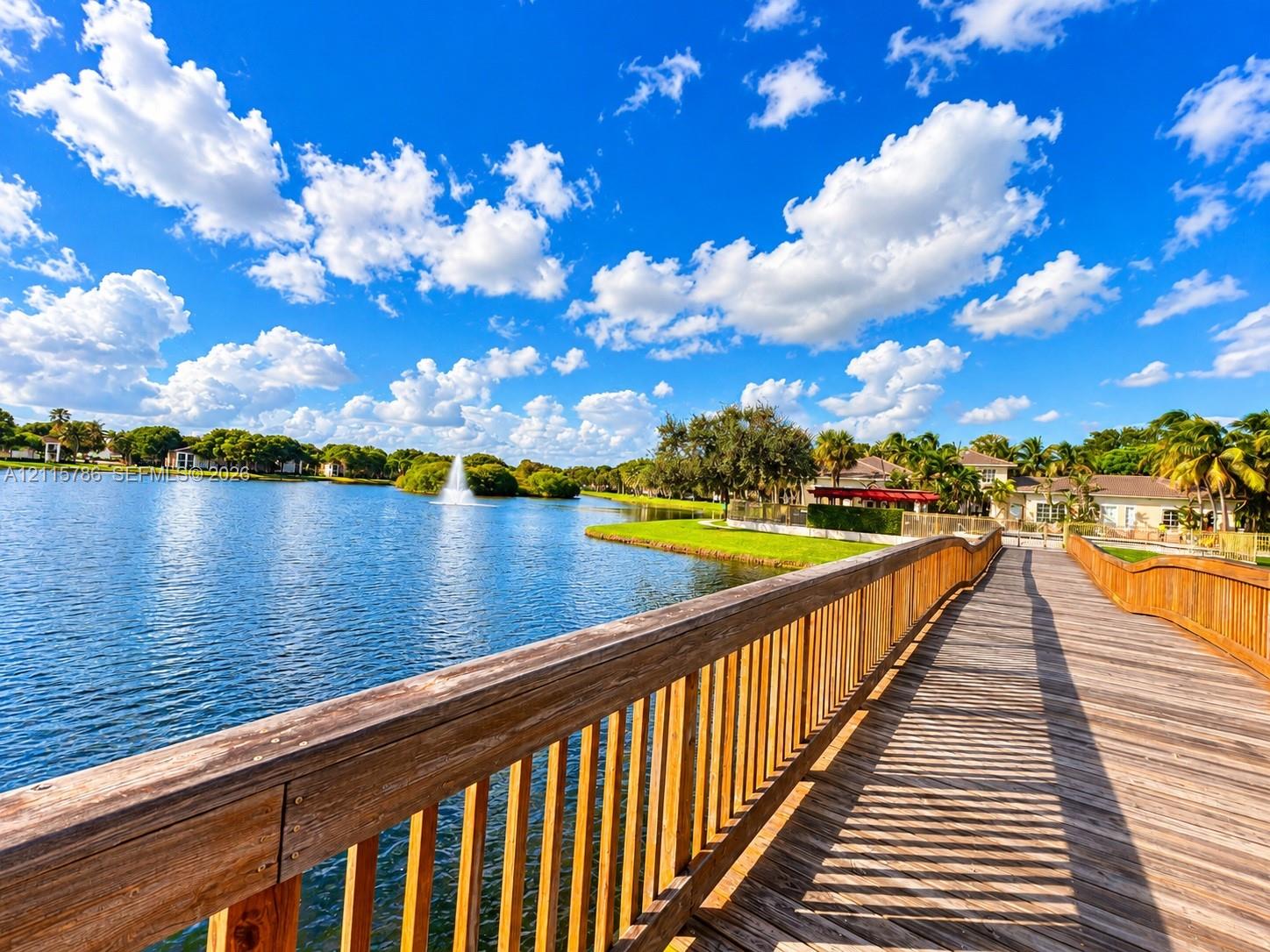 Wood-plank pedestrian bridge featuring natural wood railings, water fountain feature, and perimeter landscaping