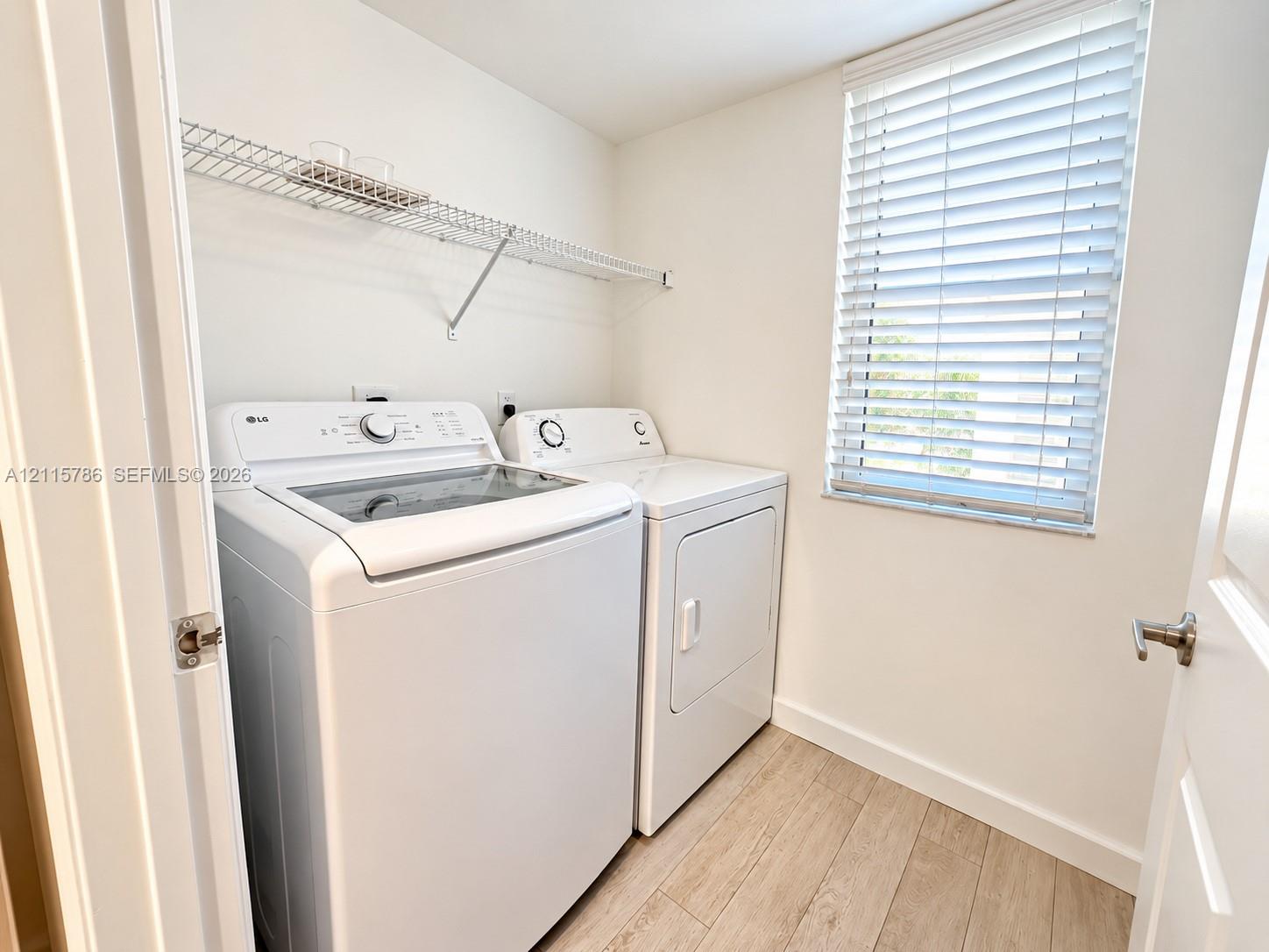 Utility room featuring wood-finish flooring, white walls, horizontal window blinds, and integrated wire shelving