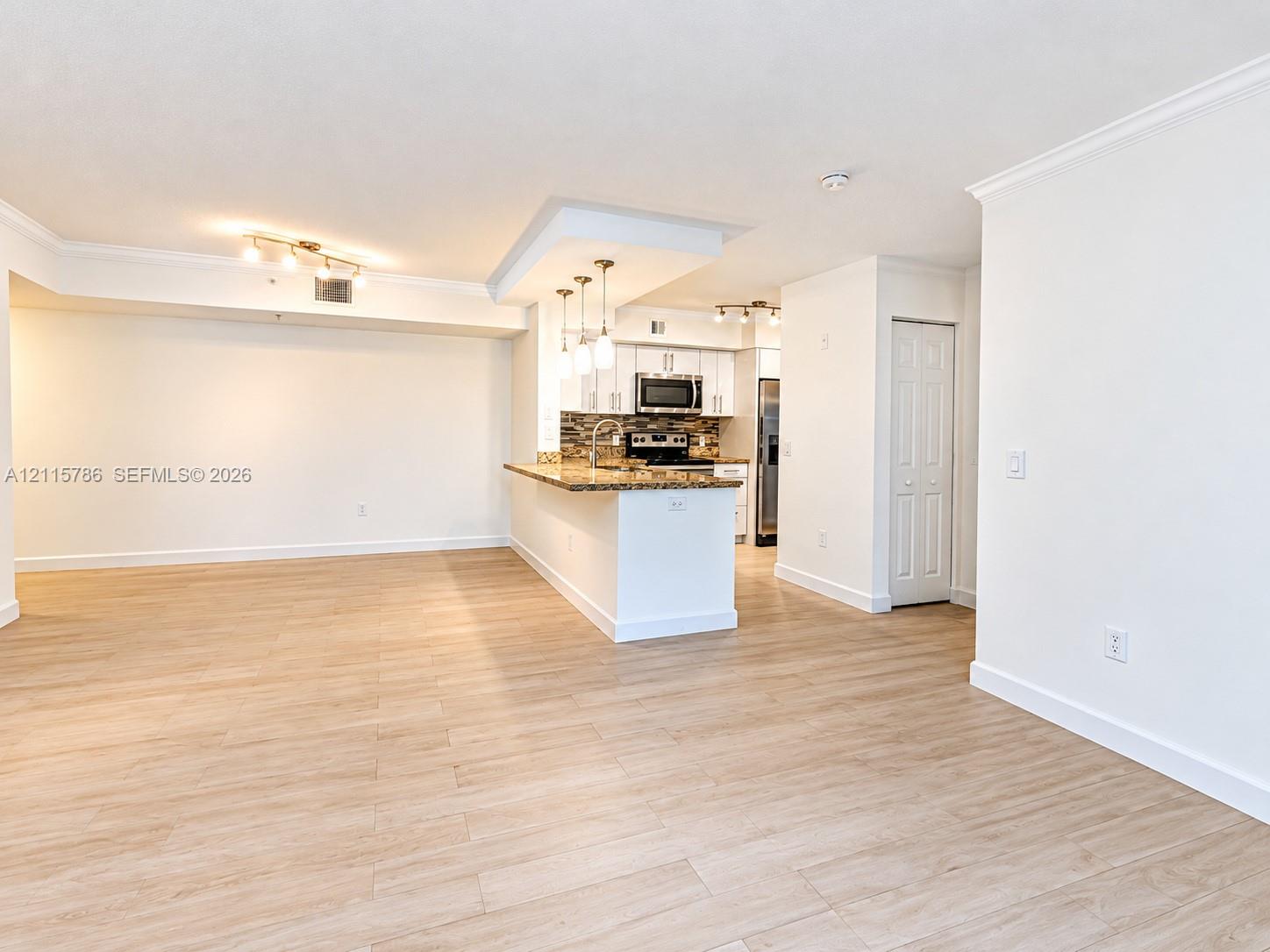 Kitchen featuring white cabinetry, stone-surface countertops, stone-tile backsplash, and stainless-steel appliances, complemented by wood-finish flooring throughout the space