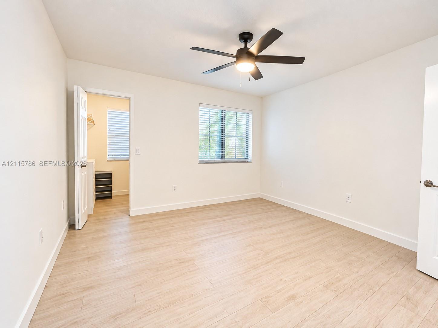 Neutral-toned interior space featuring wood-finish flooring, a ceiling fan with integrated lighting, and a multi-pane window