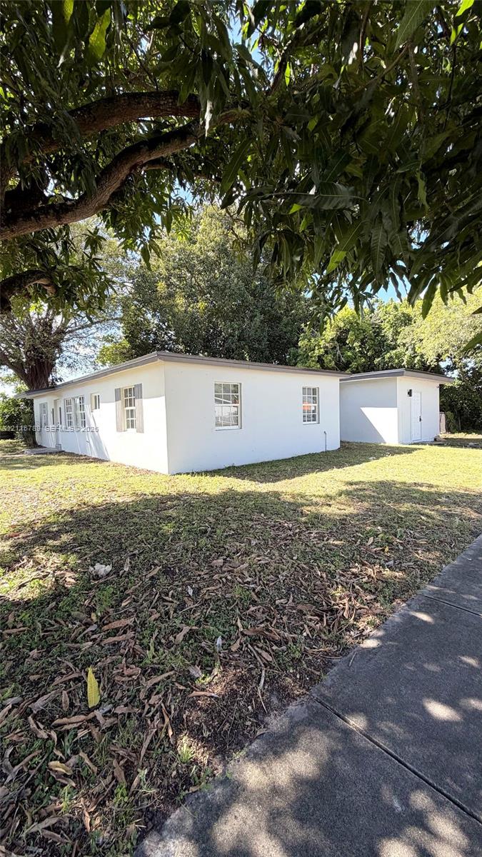 Stucco exterior featuring multi-pane windows with decorative shutters, flat roofline, and an auxiliary structure situated on a lot with mature trees