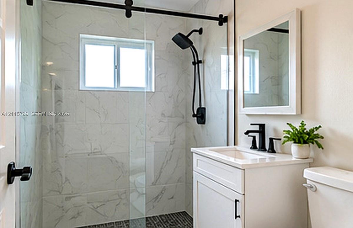 Bathroom featuring a walk-in shower with stone-patterned wall tile, a frameless glass door with matte black hardware, a black rainfall showerhead, and a vanity with a white rectangular sink