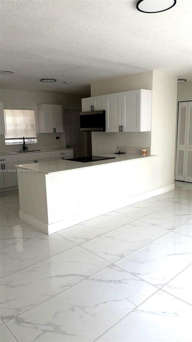 Kitchen featuring white shaker-style cabinetry, quartz countertops, a peninsula with an integrated cooktop, and large-format porcelain tile flooring