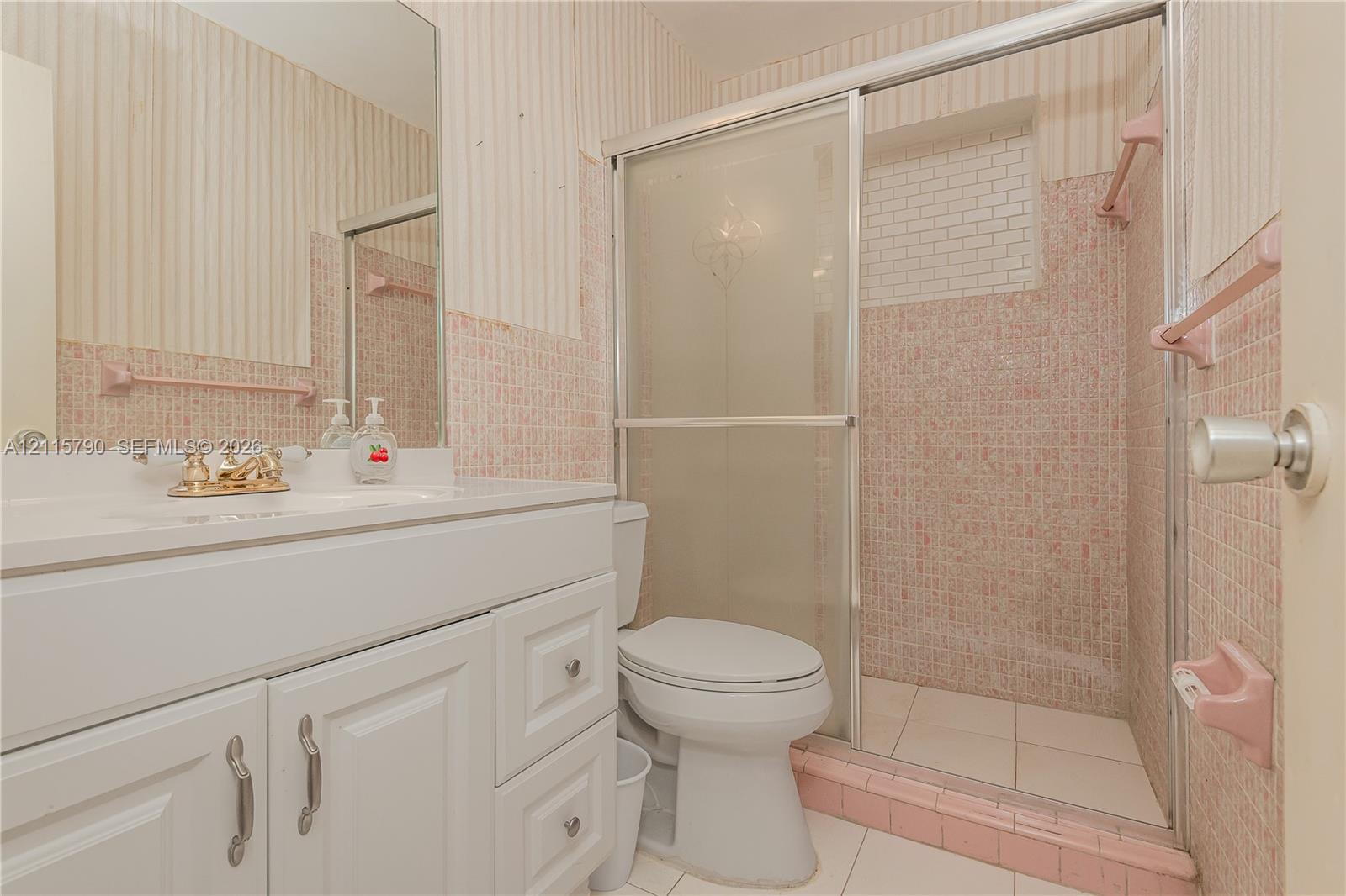 Bathroom featuring a white vanity with integrated basin, polished metal hardware, a glass-enclosed shower, tiled wall finishes, and a wall-mounted mirror