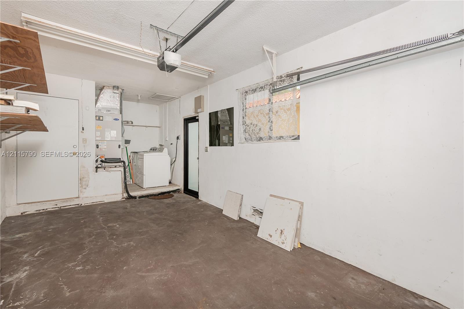 Garage space featuring concrete flooring, an overhead door motor, built-in shelving, a dedicated laundry area, and a glass-paneled entry door