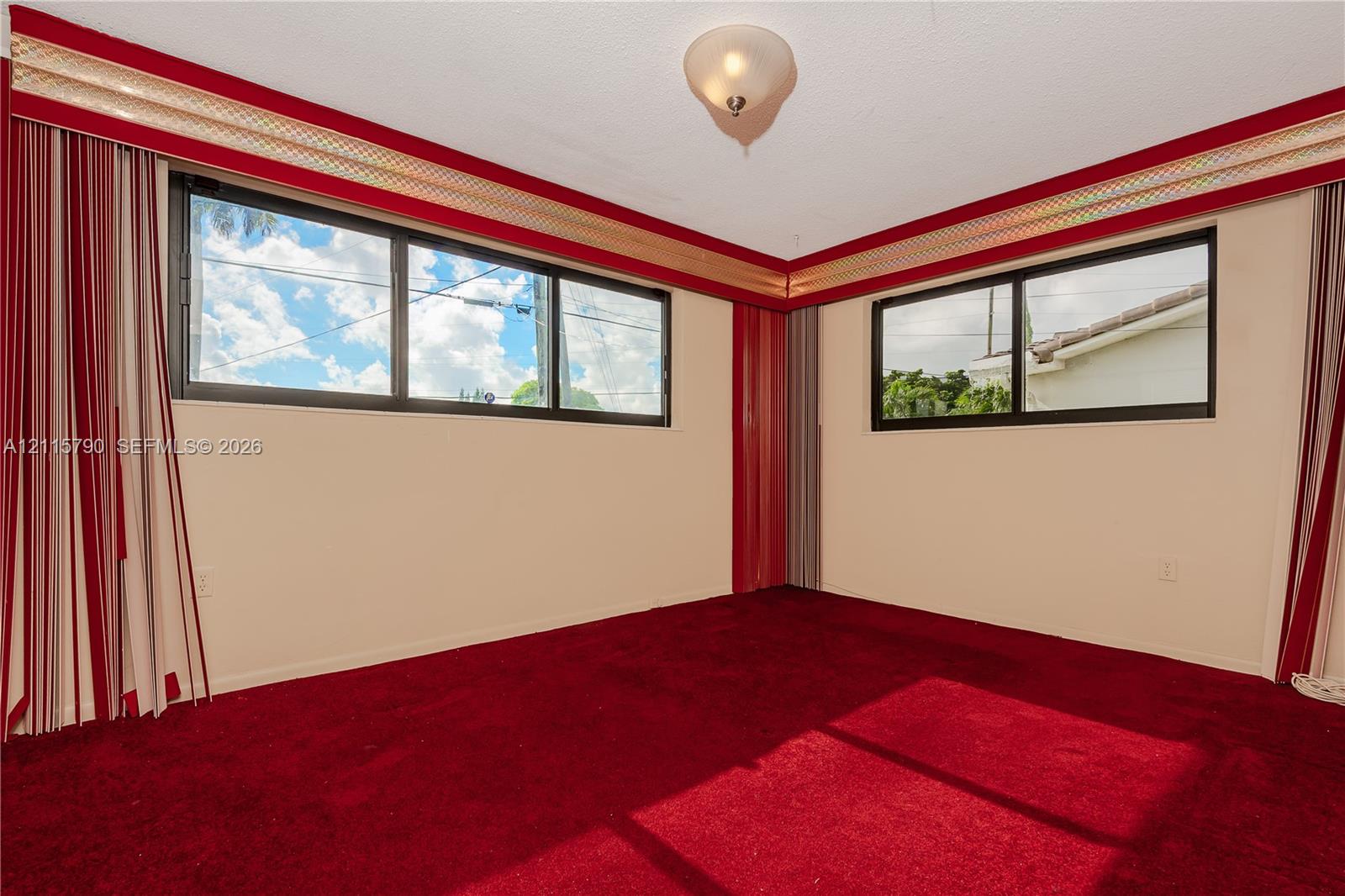 Corner room featuring dual-aspect horizontal windows, ceiling-mounted flush light fixture, and wall-to-wall carpeting