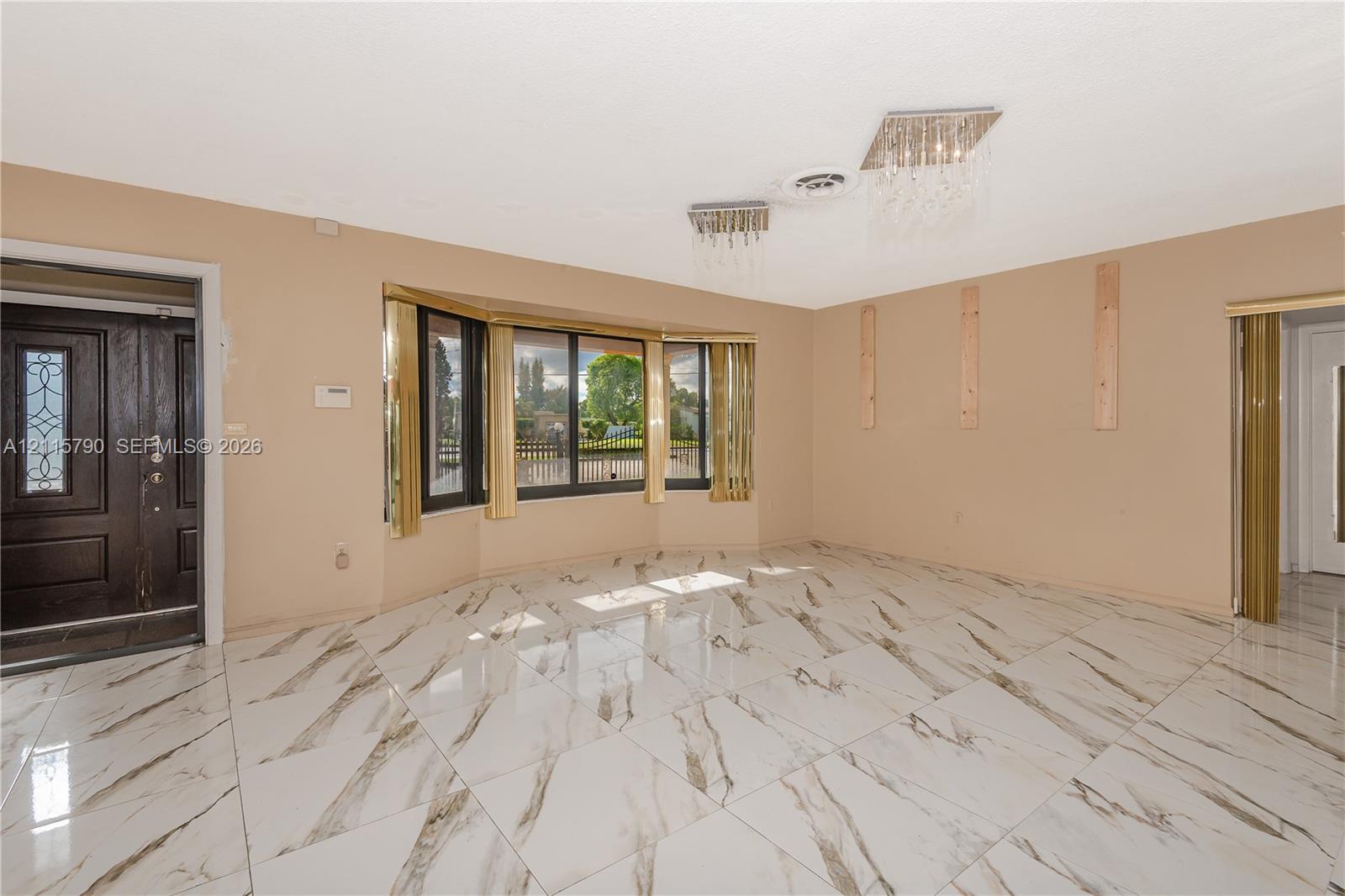 Large-format stone-style tile flooring, expansive bay window, ornate crystal-style ceiling light fixtures, and solid-core dark wood entry door with decorative glass inlay
