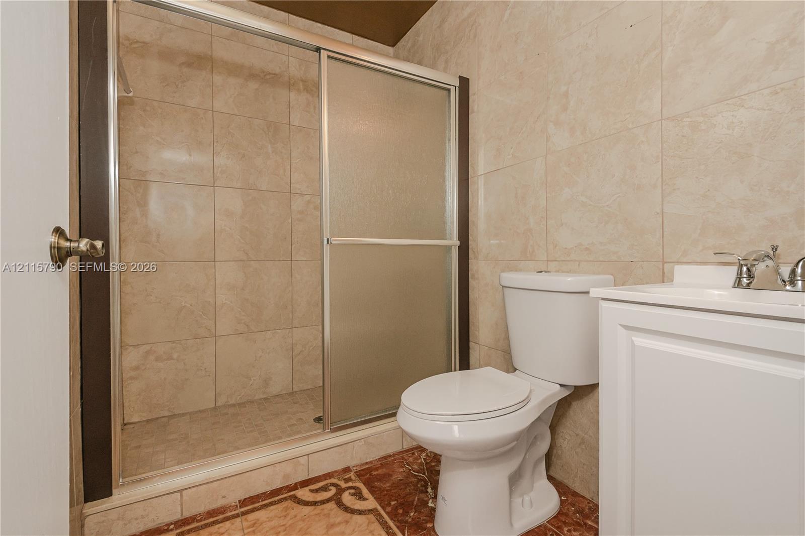 Walk-in shower with sliding glass enclosure and tiled surround, white vanity, and toilet