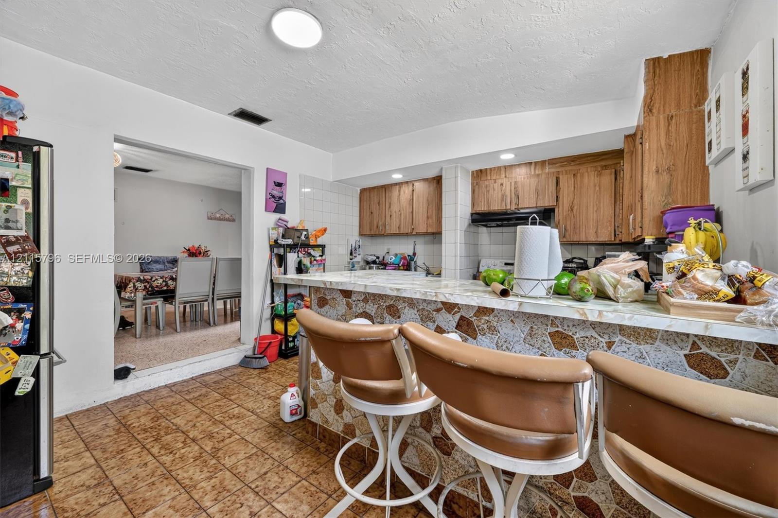 Kitchen featuring wood cabinetry, a stone-patterned bar counter with stone-tile facade, and ceramic floor tile