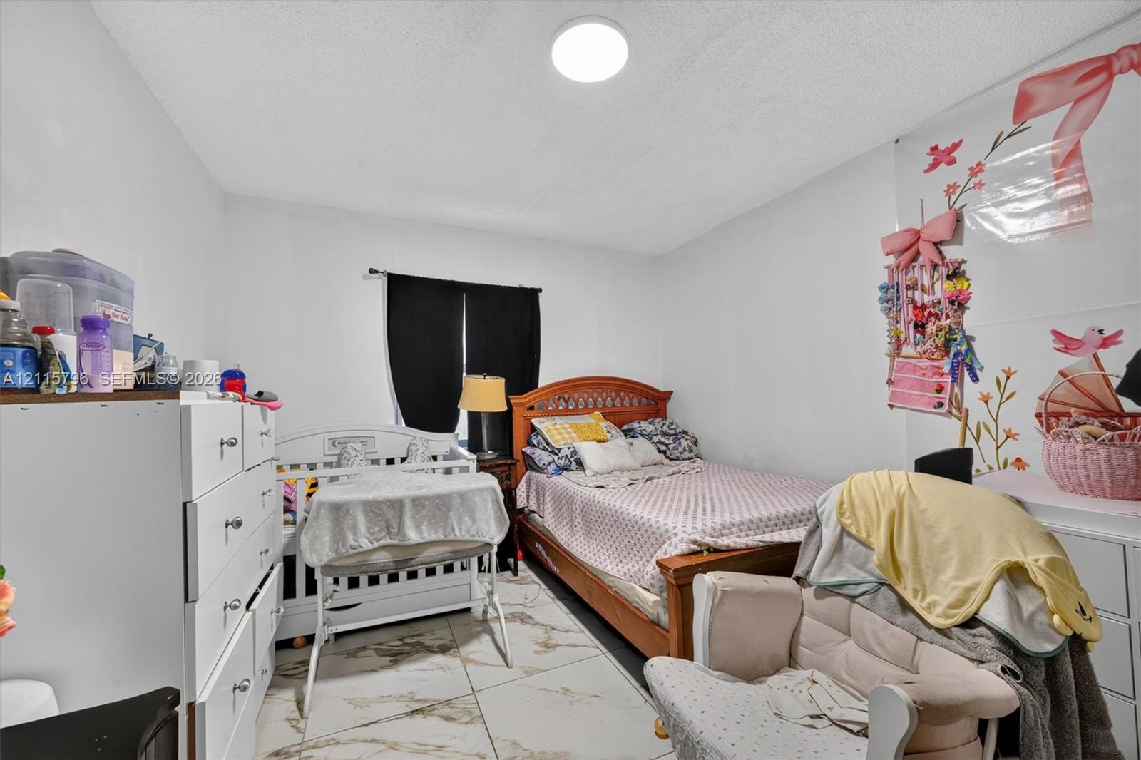 Large-format neutral tile flooring throughout the room and a flush-mount circular ceiling light fixture