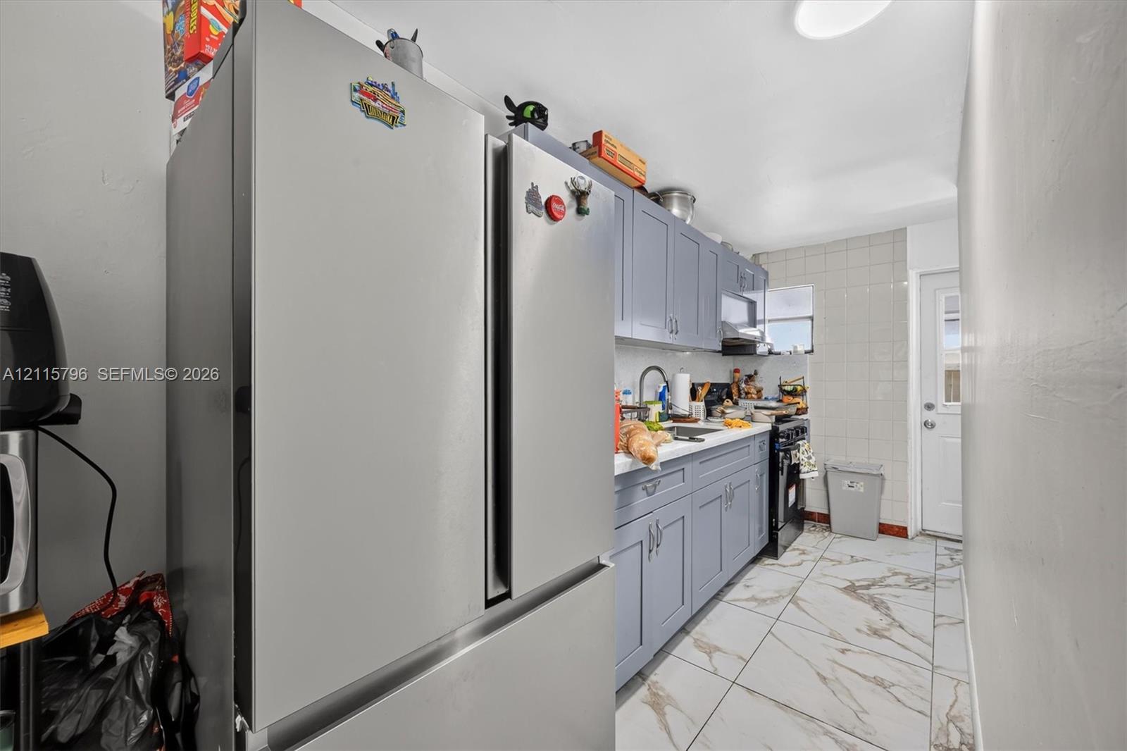 Kitchen featuring grey shaker-style cabinetry, stainless steel french-door refrigerator, tile backsplash, stone-finish floor tile, and exterior access door