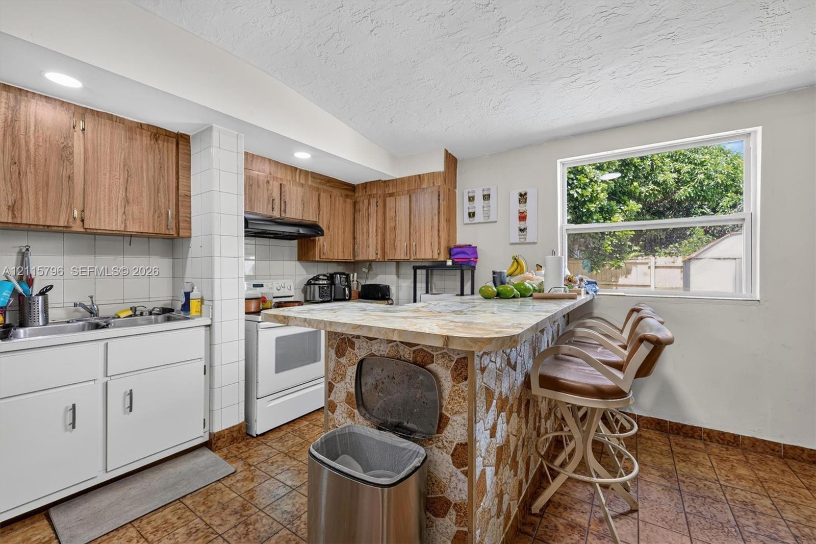 Kitchen featuring wood-finish upper cabinetry, white lower cabinetry, tile-topped peninsula with stone-finish base, and recessed lighting