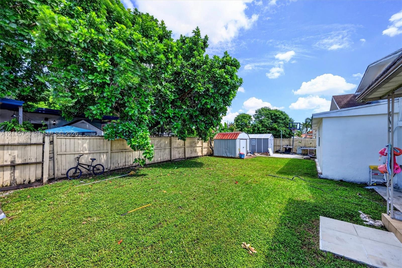 Expansive backyard featuring a manicured lawn, perimeter wood fencing, and two detached metal storage structures