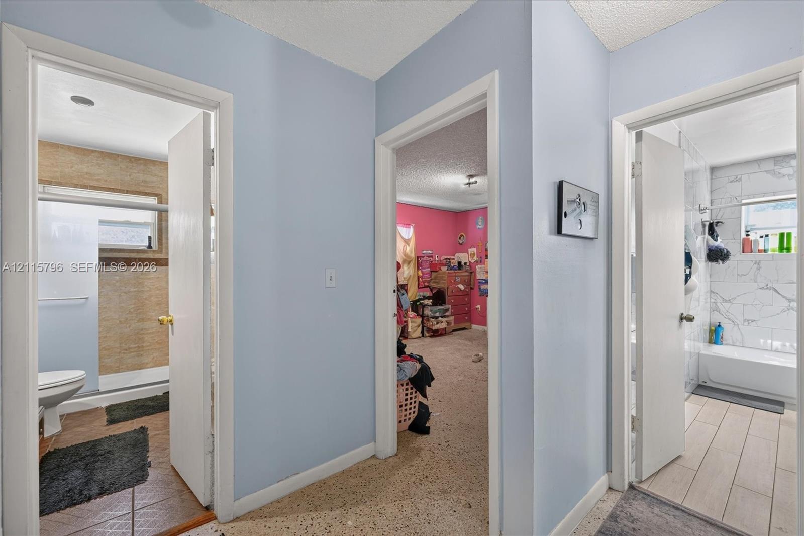 Hallway featuring neutral wall tones, textured ceiling, tiled flooring, and multiple interior doorways providing access to finished rooms with varied tile and surfacing materials