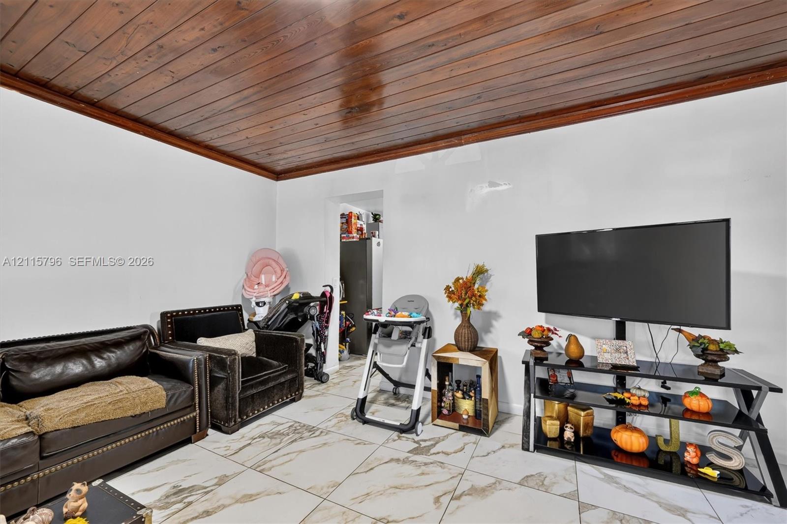 Room featuring a tongue-and-groove wood plank ceiling and large-format tile flooring with marble-patterned detailing