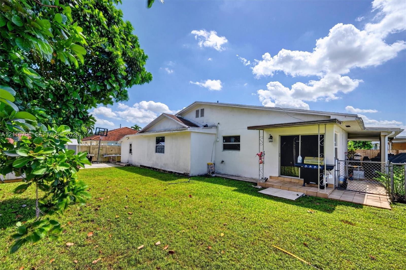 Exterior view featuring a grass lawn, tiled patio, covered porch, and chain-link perimeter fencing