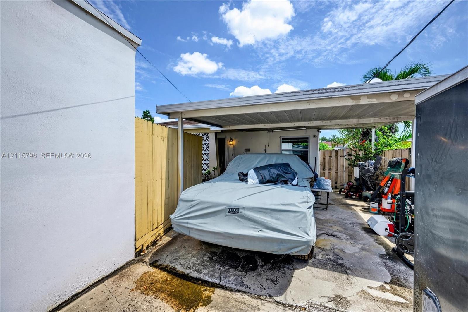 Covered carport with concrete flooring, enclosed by wood privacy fencing and exterior wall cladding