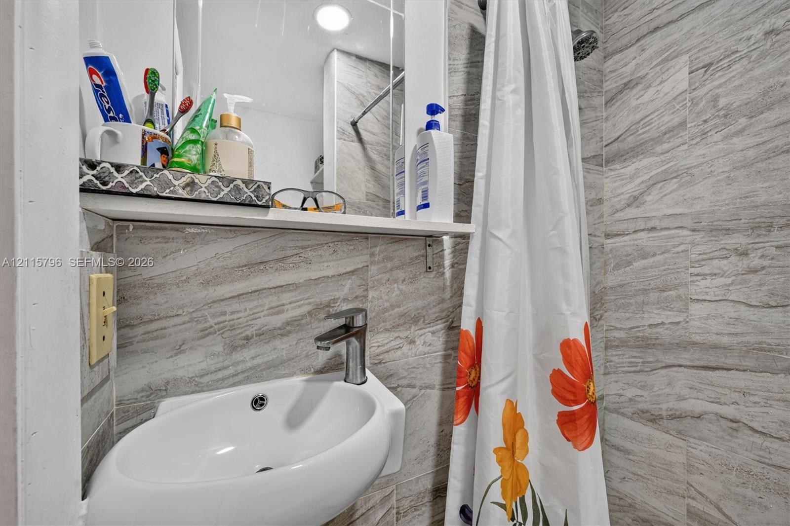 Wall-mounted ceramic sink with a single-handle metal faucet, accented by stone-finish wall tile and a built-in recessed mirror