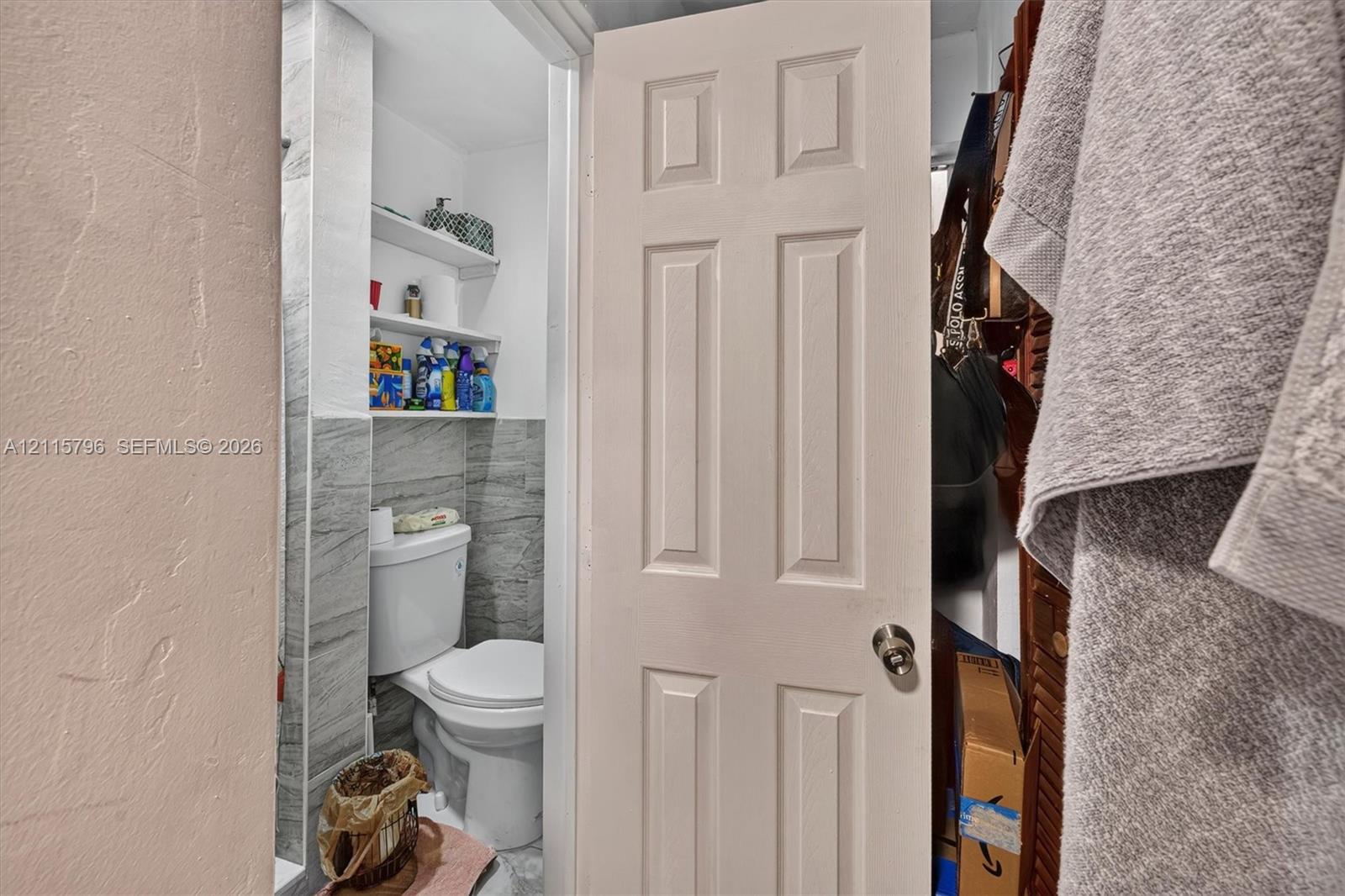 Bathroom featuring gray stone-patterned wall tile, two built-in storage shelves, and a standard-height toilet