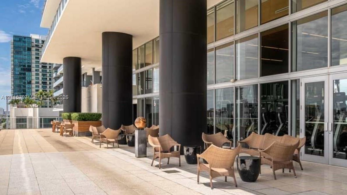 Expansive outdoor terrace featuring stone tile flooring, prominent structural columns, and floor-to-ceiling glass wall panels