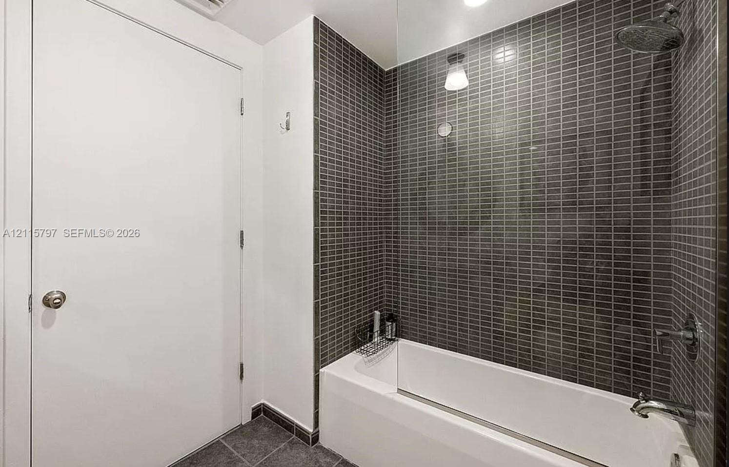 Bathtub featuring a glass shower panel, charcoal-toned mosaic tile surround, and polished chrome rainfall showerhead