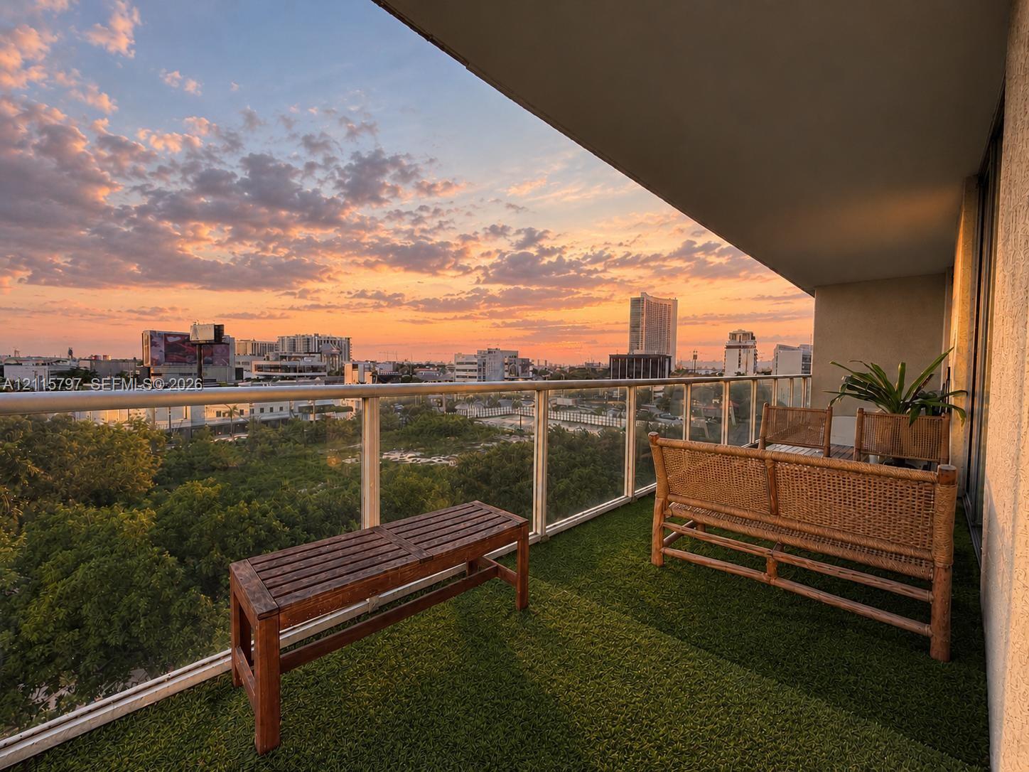 Covered balcony featuring a glass panel railing, artificial turf surfacing, and expansive urban scenery