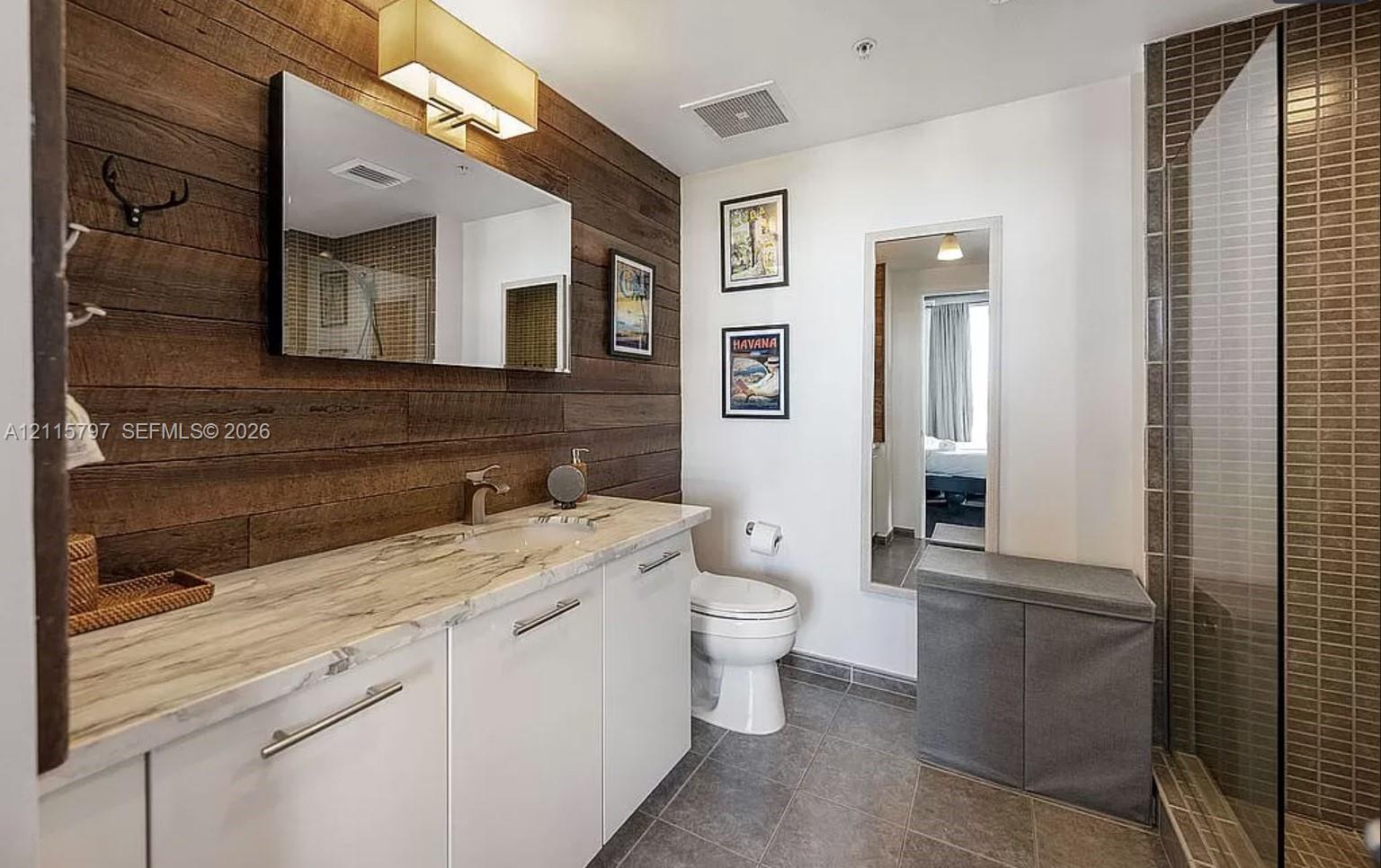 Bathroom featuring a wood-plank accent wall, white cabinetry with stone-finish countertop, undermount sink with metallic faucet, and a tiled walk-in shower