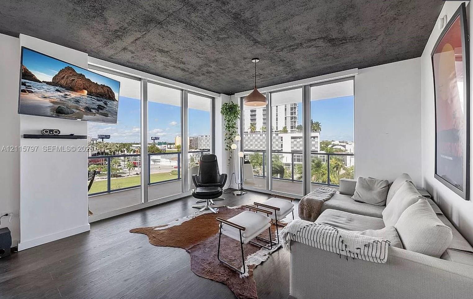 Floor-to-ceiling windows, exposed concrete ceiling, dark wood-finish flooring, and a private balcony