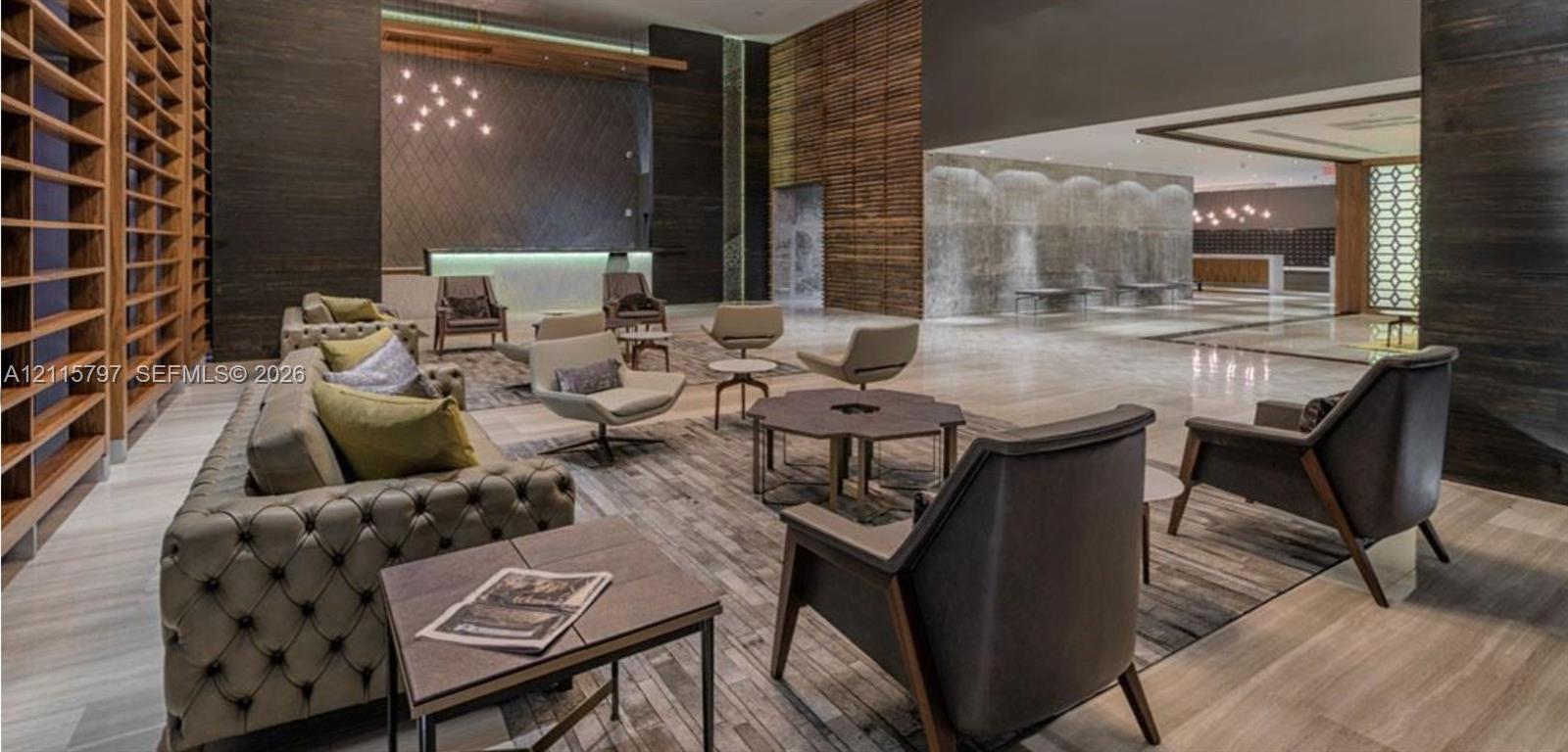 Double-height ceiling lobby featuring stone-surround wall paneling, built-in floor-to-ceiling wooden shelving, polished stone flooring, and a decorative interior water feature