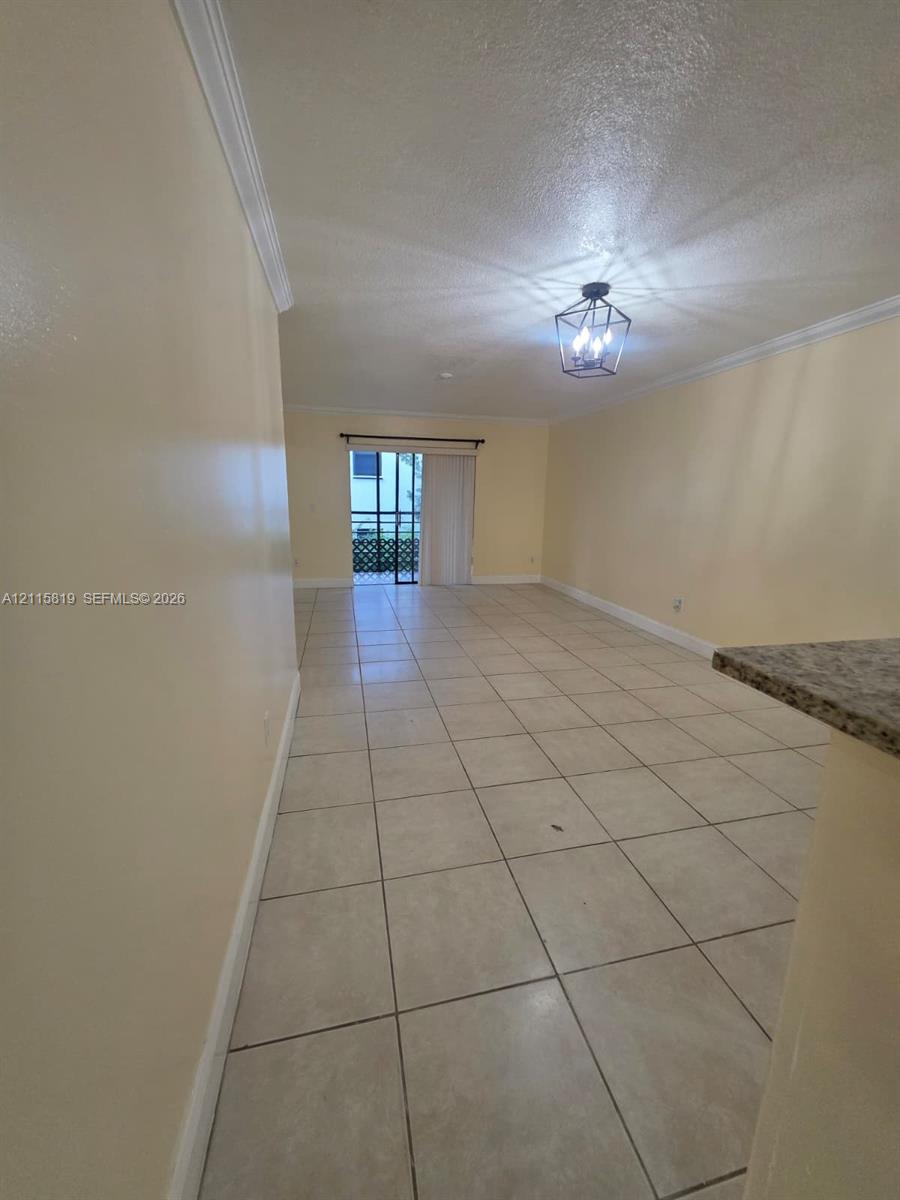 Neutral tile flooring, crown molding, modern geometric cage-style chandelier, and sliding glass door with exterior access