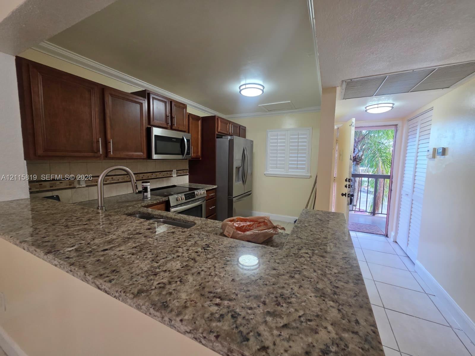 Kitchen featuring stone countertops, dark wood-finish cabinetry, stainless steel appliances, a high-arc faucet, and tile flooring