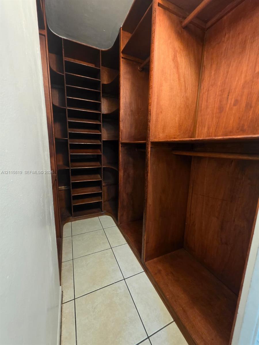 Custom wood-finish cabinetry featuring integrated shelving, vertical storage compartments, and hanging rods, complemented by tile flooring