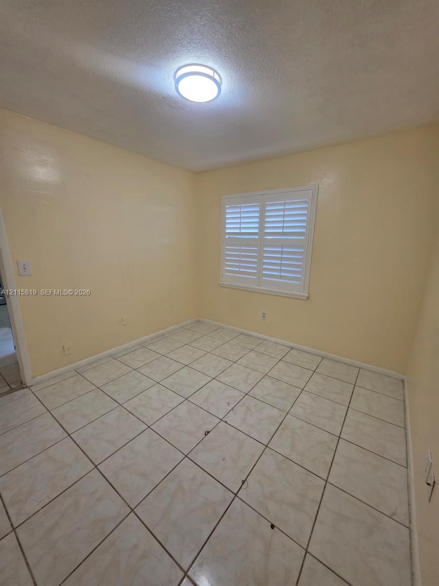 Interior room featuring large-format ceramic tile flooring, neutral wall tones, and white plantation shutters