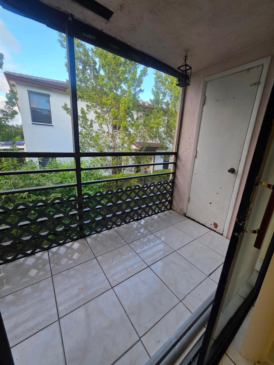 Screened balcony featuring ceramic tile flooring, a black metal lattice railing, and a private storage closet