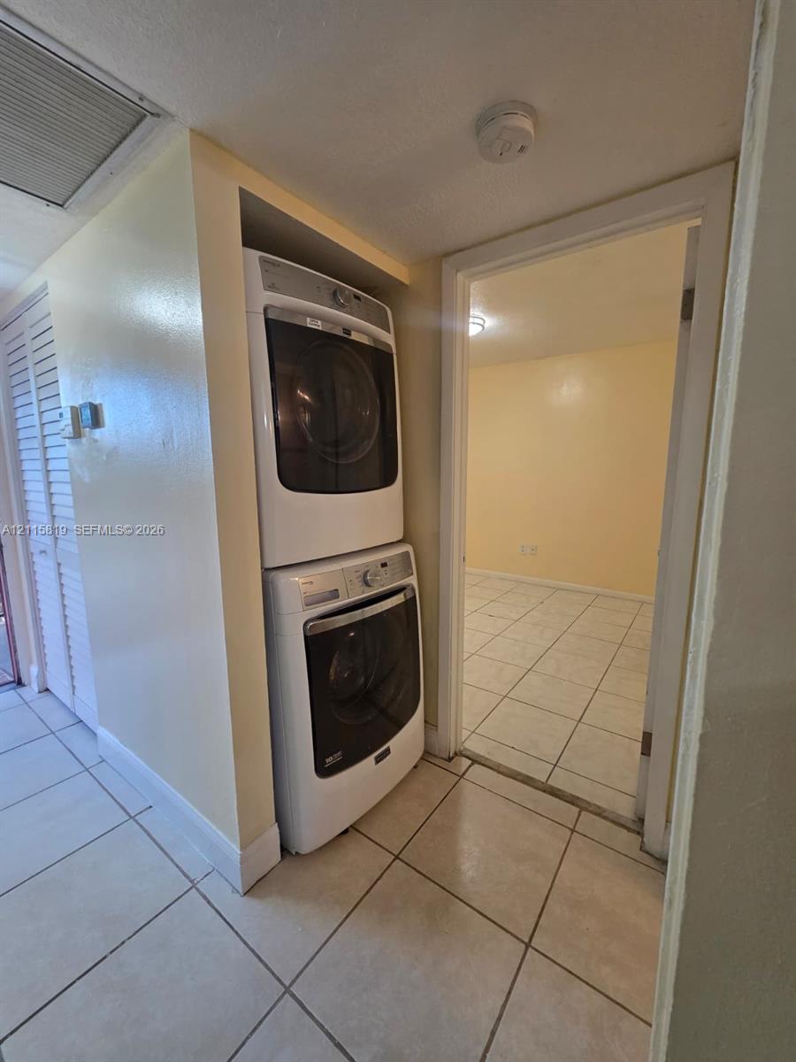 Stacked white front-load washer and dryer unit with ceramic tile flooring