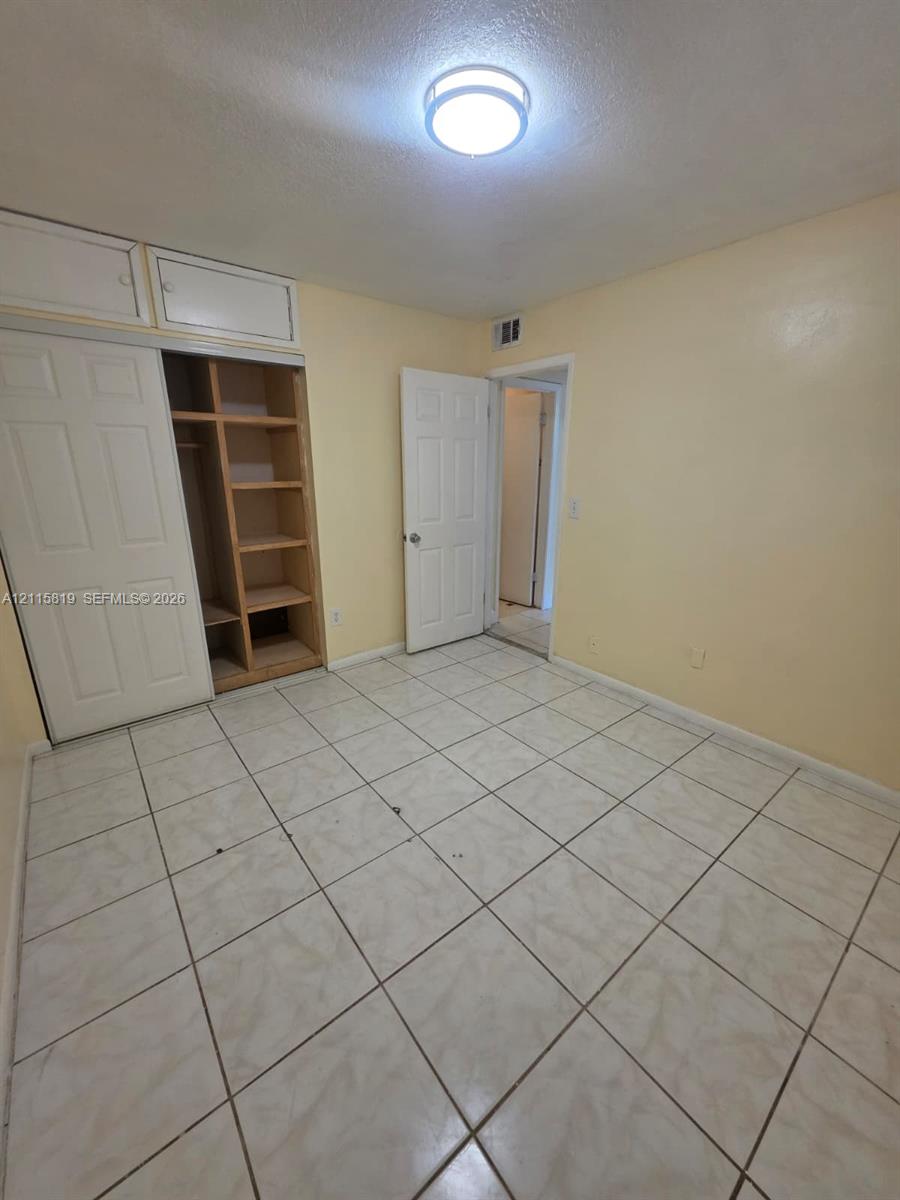Room featuring neutral tile flooring, built-in shelving with overhead storage cabinets, and a flush-mount ceiling light fixture