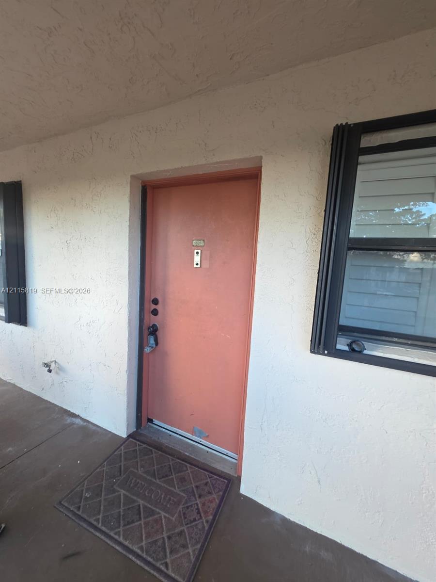 Exterior entry featuring a solid door, integrated door knocker, and metal-framed window with exterior casing