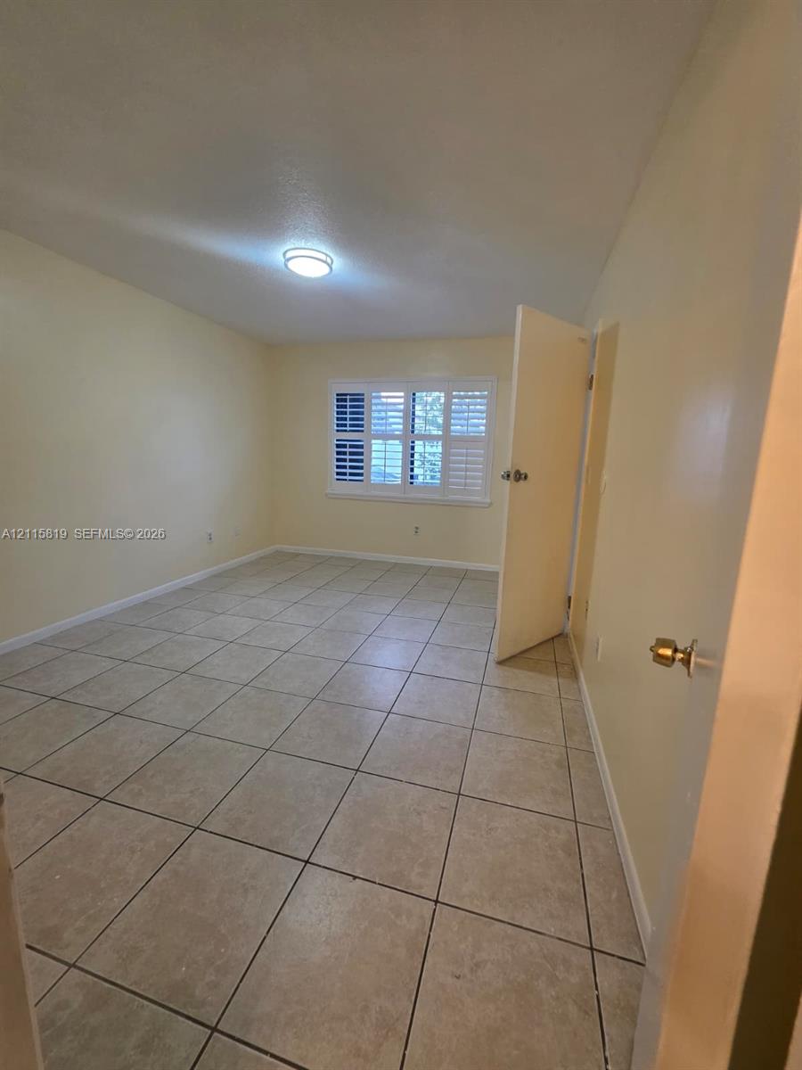 Room featuring neutral tile flooring, window with interior shutters, and ceiling-mounted lighting