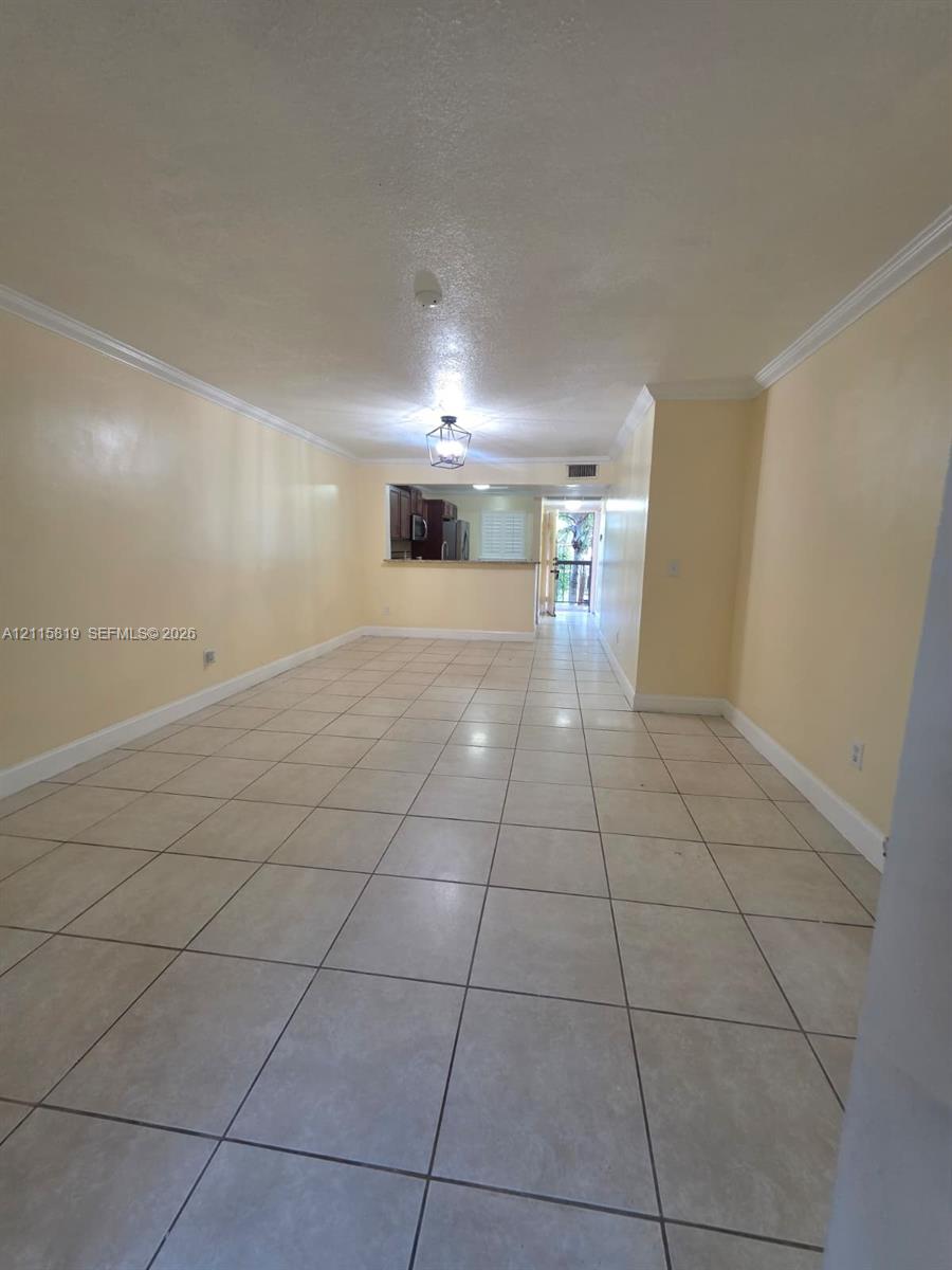 Open-concept area featuring light-toned tile flooring, crown molding, and a pass-through opening into the kitchen area with a ceiling-mounted lantern light fixture