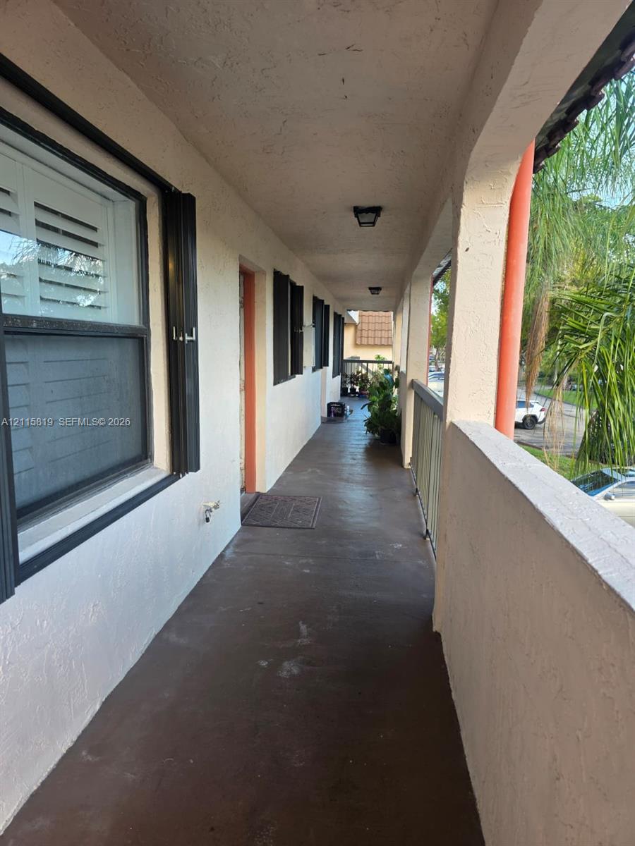 Covered exterior walkway featuring stucco walls, flush-mount lighting, dark-toned concrete flooring, and metal railings