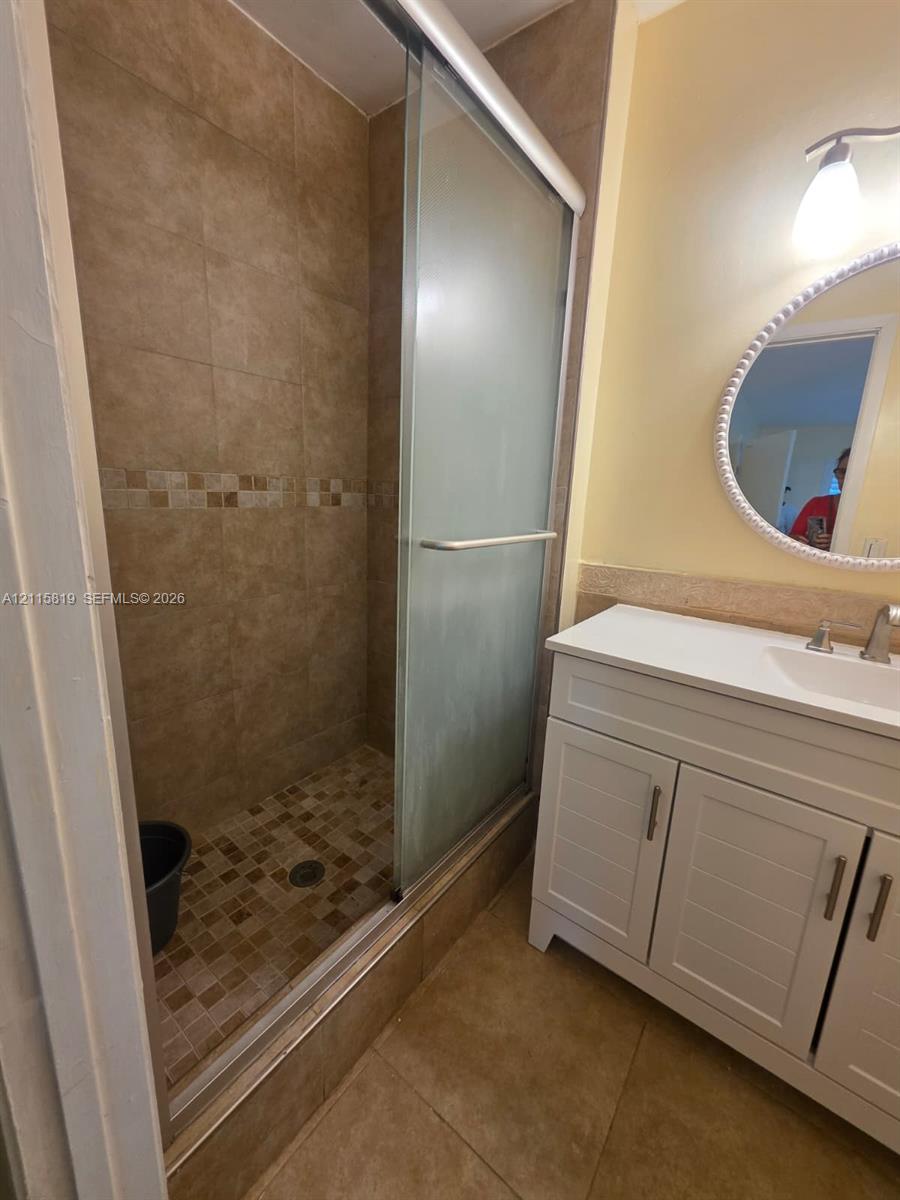 Bathroom featuring a walk-in shower with a glass sliding door, mosaic tile flooring, neutral wall tiling, white cabinetry, and a countertop-integrated sink